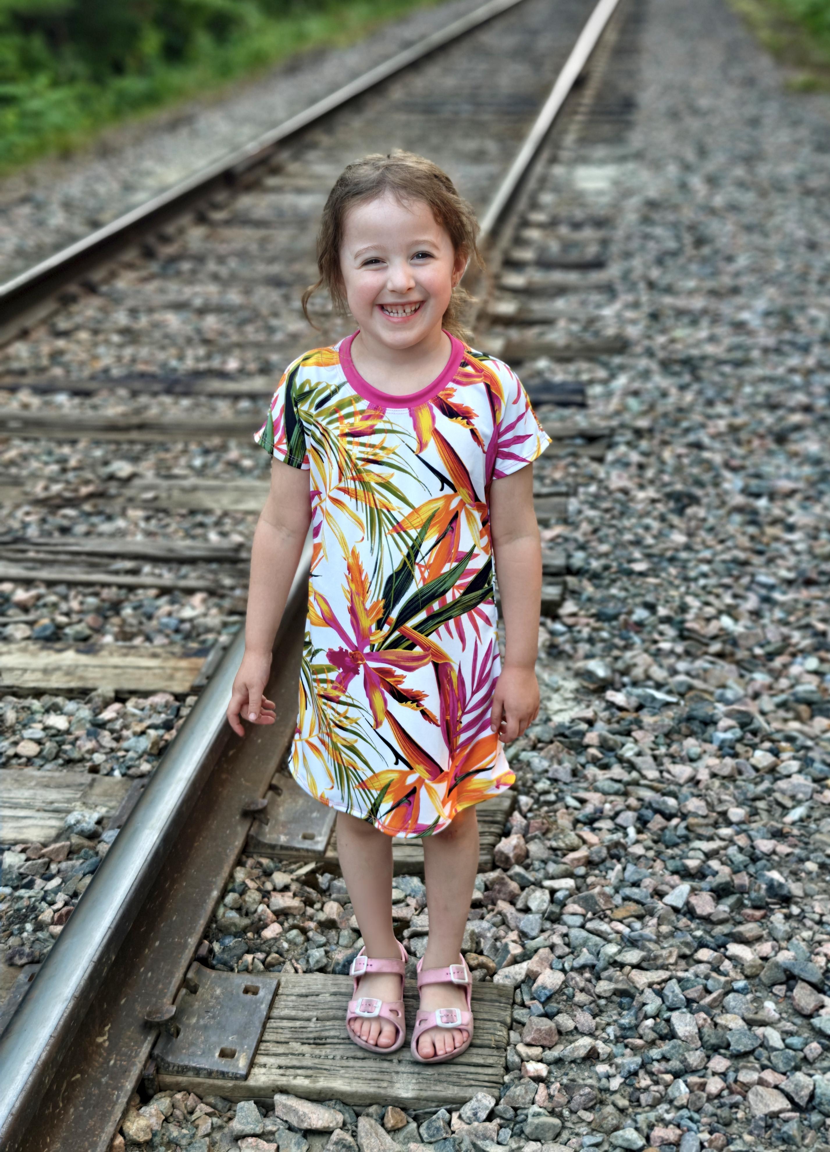 Young girl in a colorful dress standing on train tracks