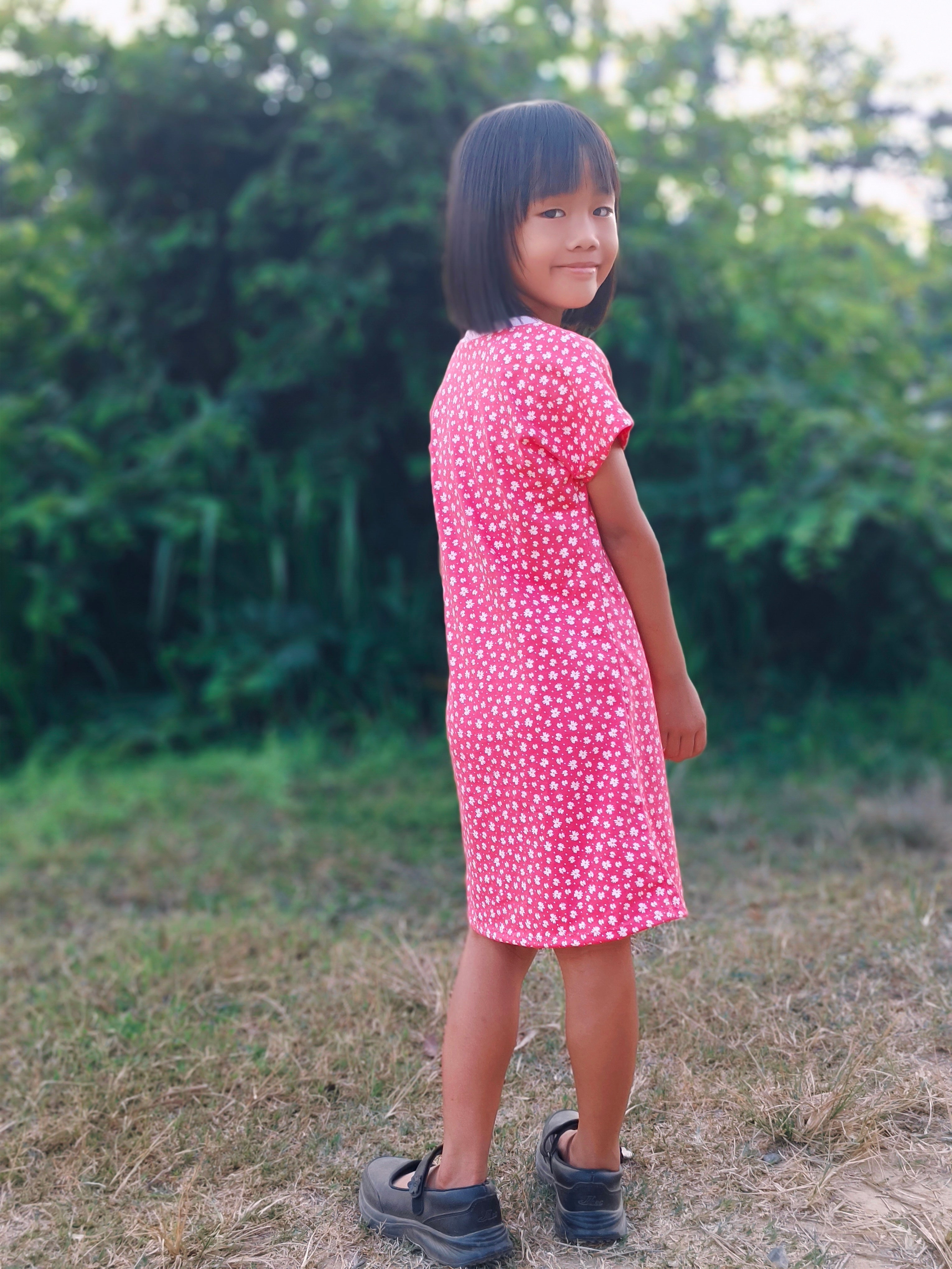 Person wearing a pink dress with white polka dots standing outdoors with trees in the background