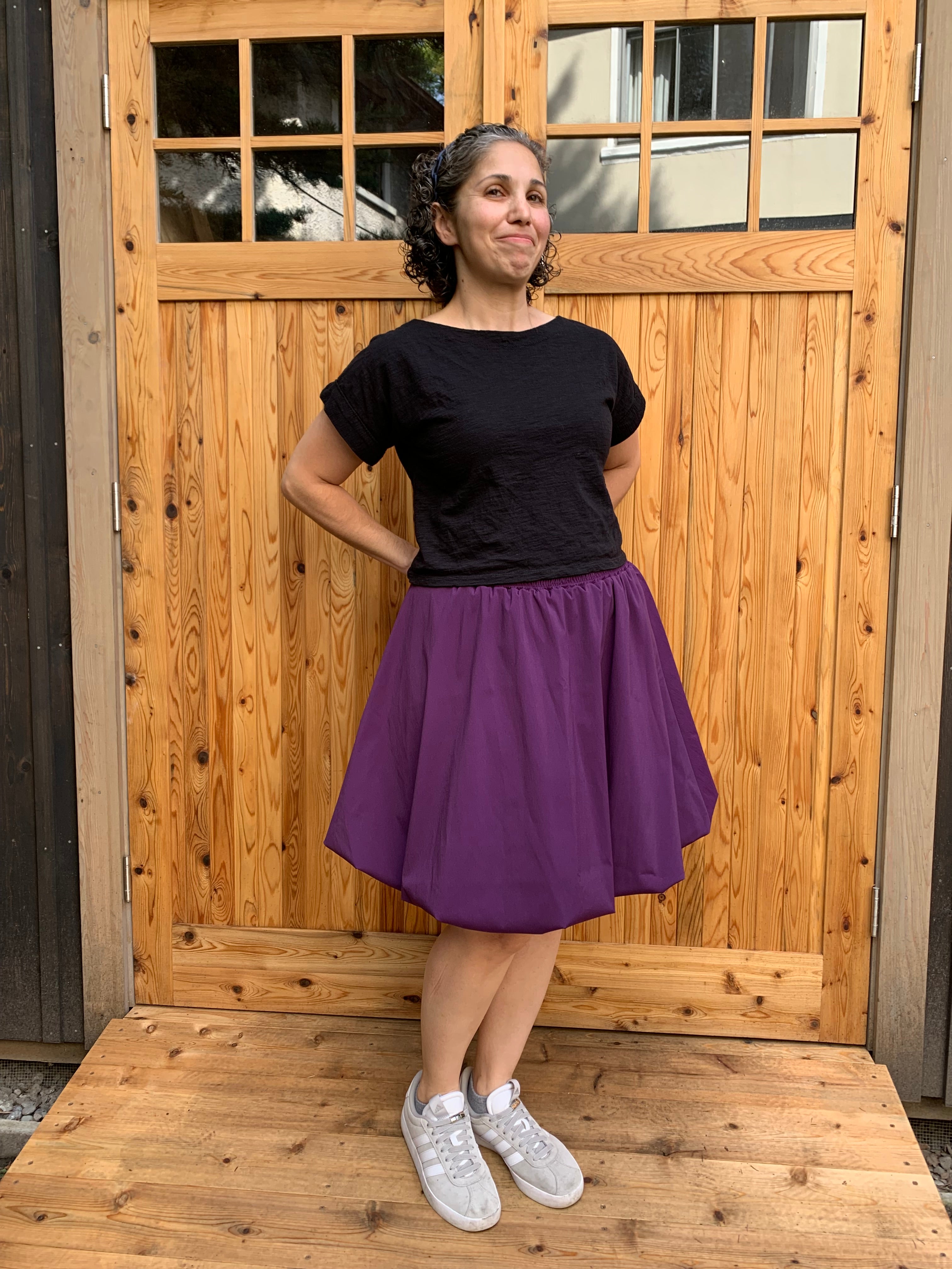 Person wearing a black top and purple athletic fabric bubble skirt standing on a wooden floor.
