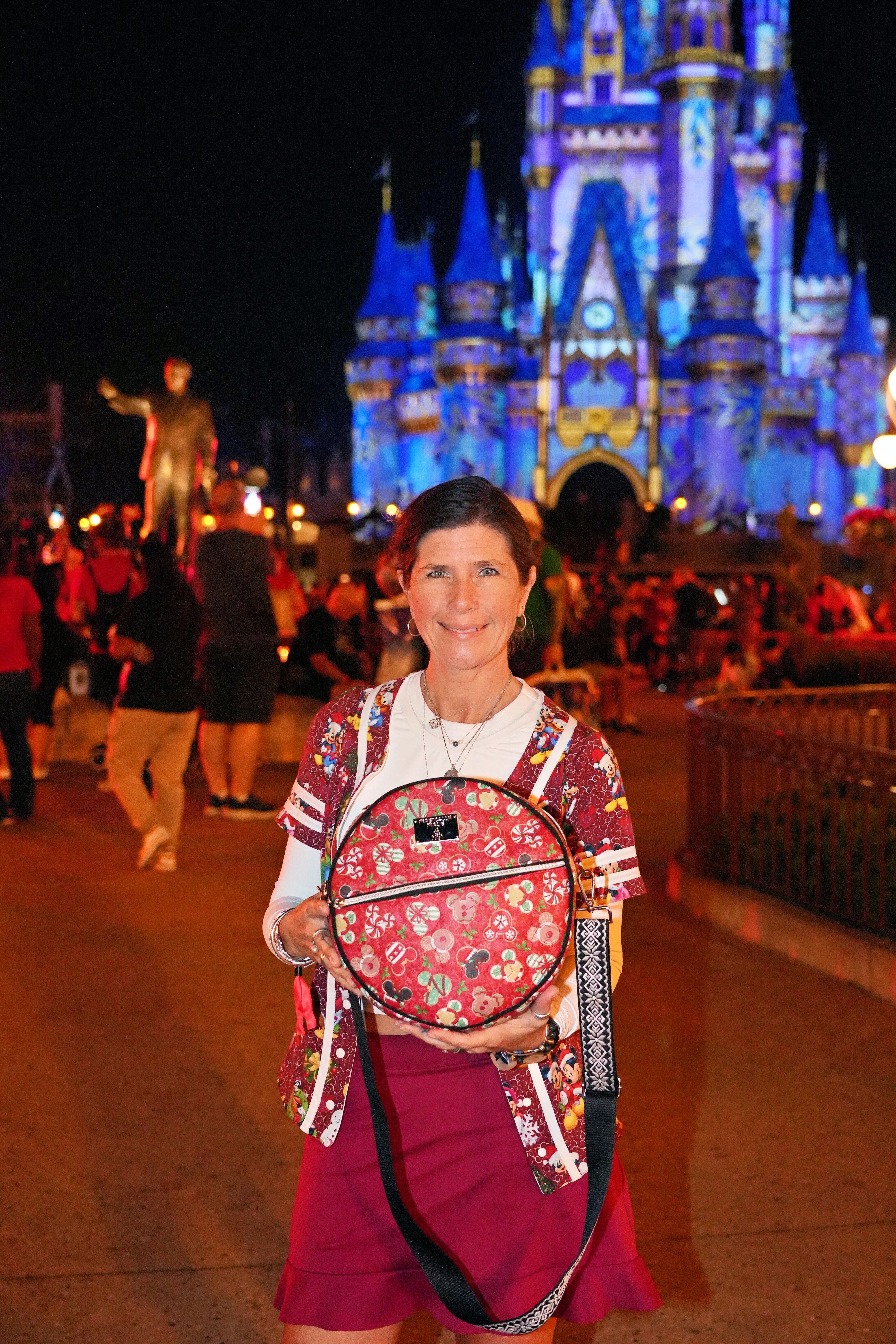 Person holding a backpack with Cinderella Castle in the background at night.