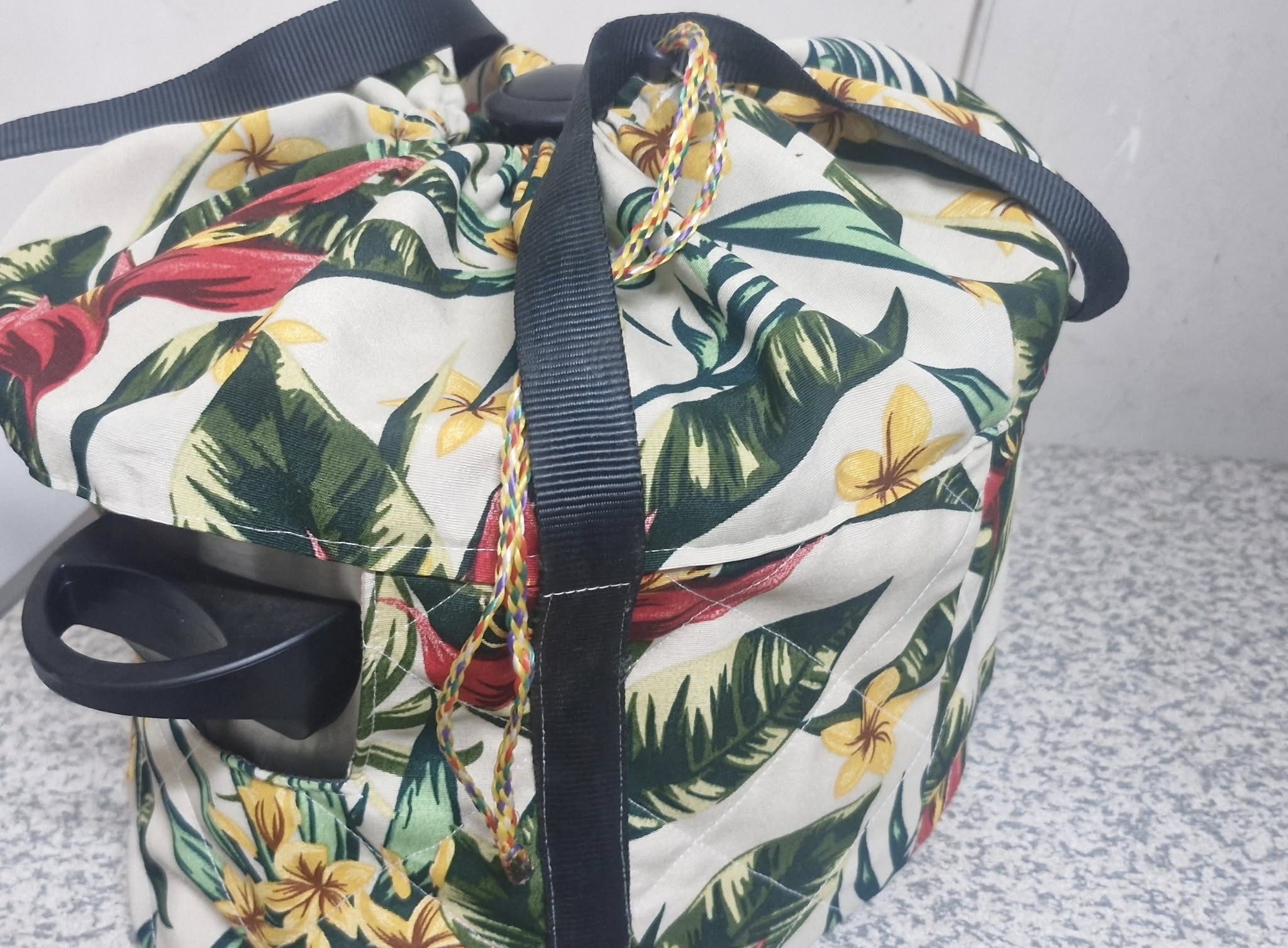 Floral-patterned crock pot insulated bag with black straps on a textured surface.
