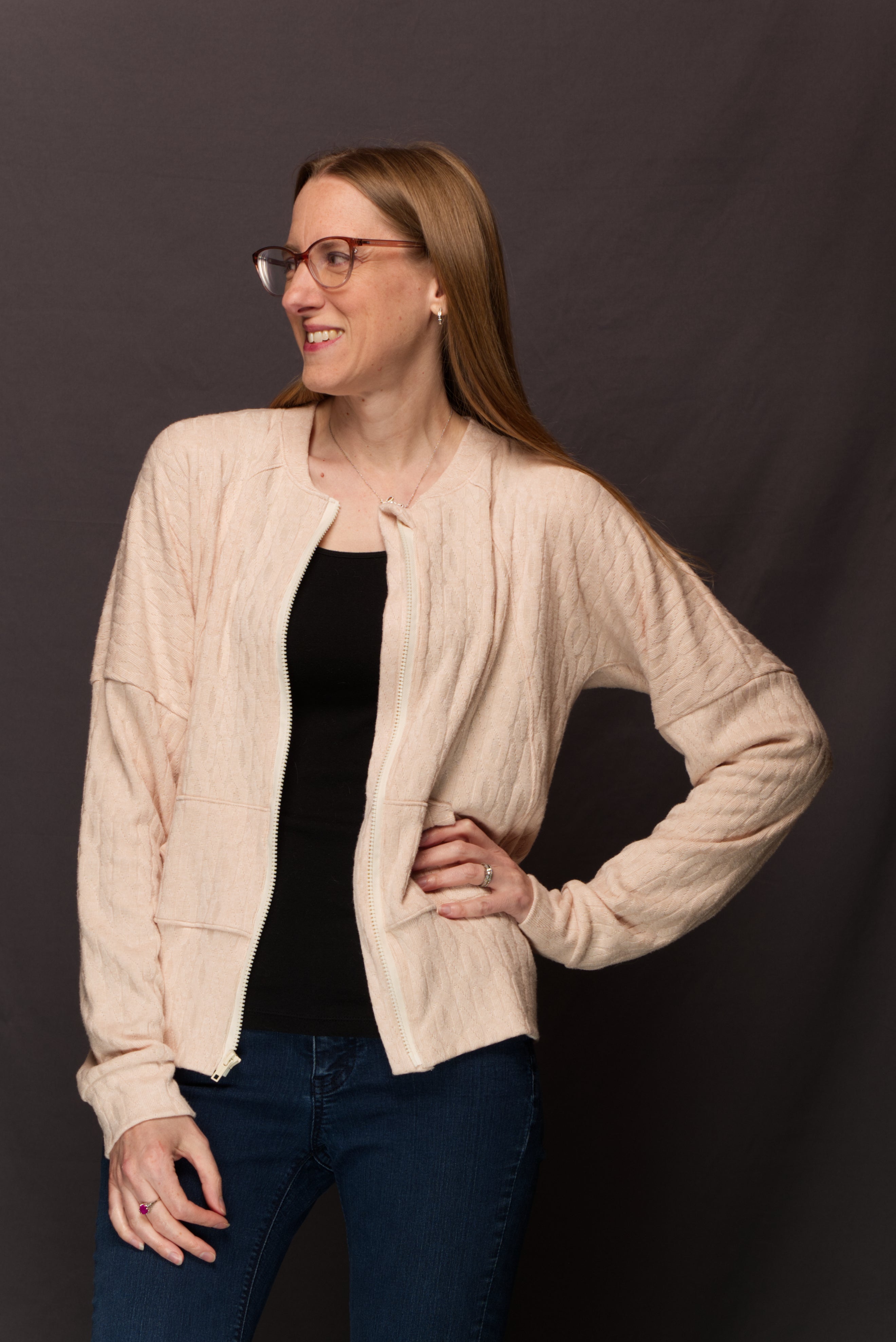 Woman wearing a sweater knit fabric zip-up jacket with raglan dolman sleeves, kangaroo pocket, and curved waistband. Knit fabric sewing pattern - instant download. High Hip Version.