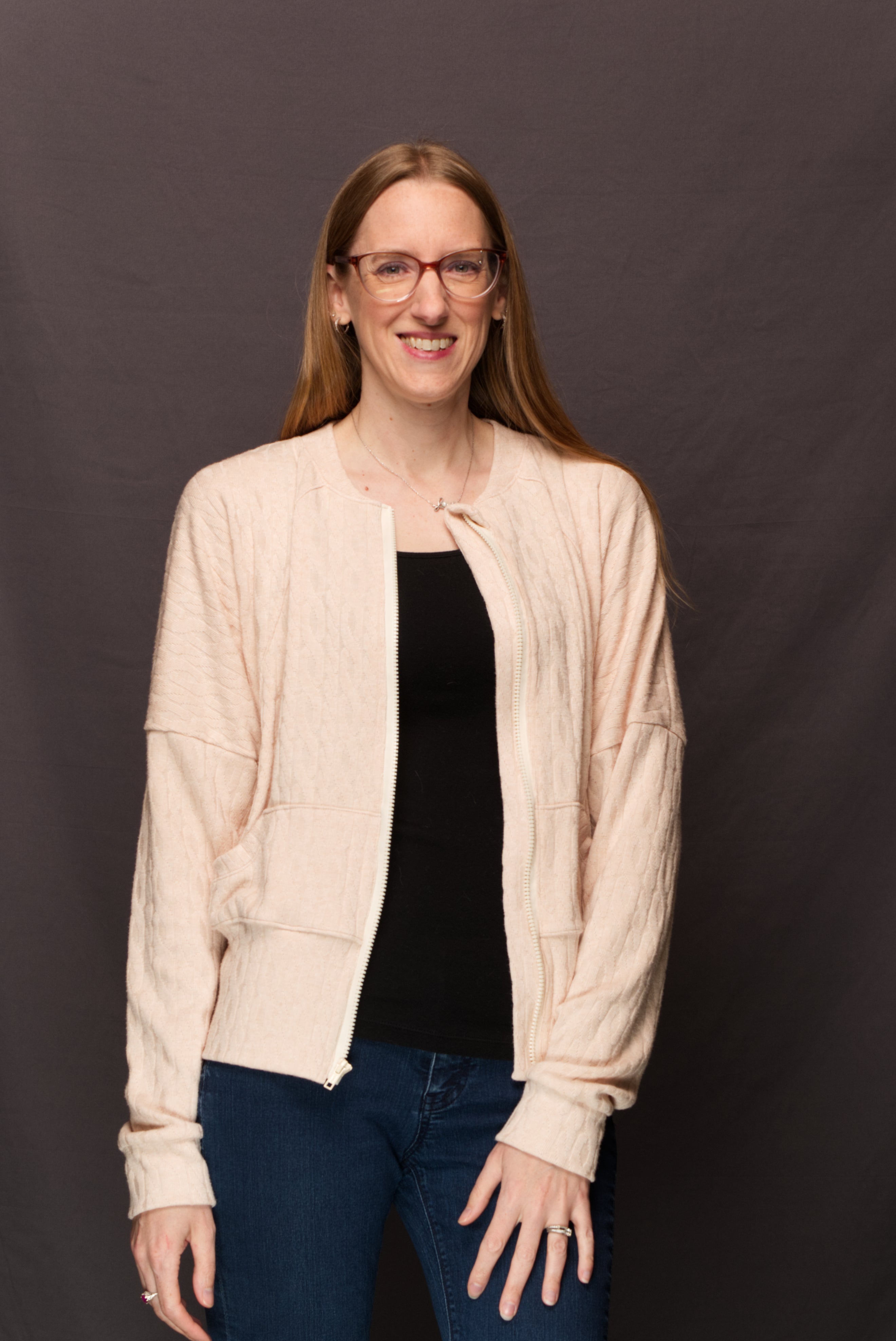 Woman wearing a sweater knit fabric zip-up jacket with raglan dolman sleeves, kangaroo pocket, and curved waistband. Knit fabric sewing pattern - instant download. High Hip Version.