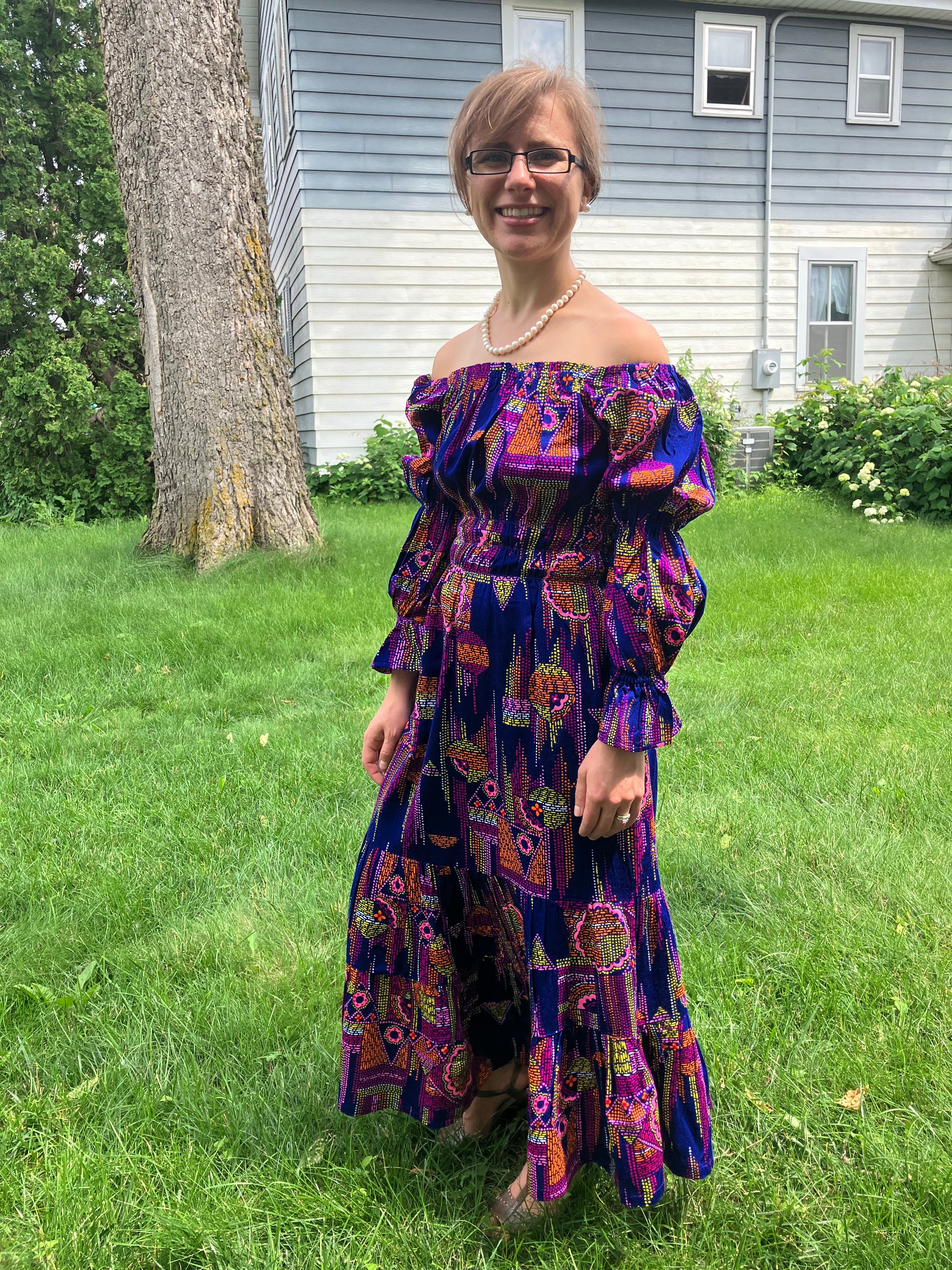 Woman in a colorful dress standing on grass next to a house. This dress is made using the Ellie and Mac sewing patterns.