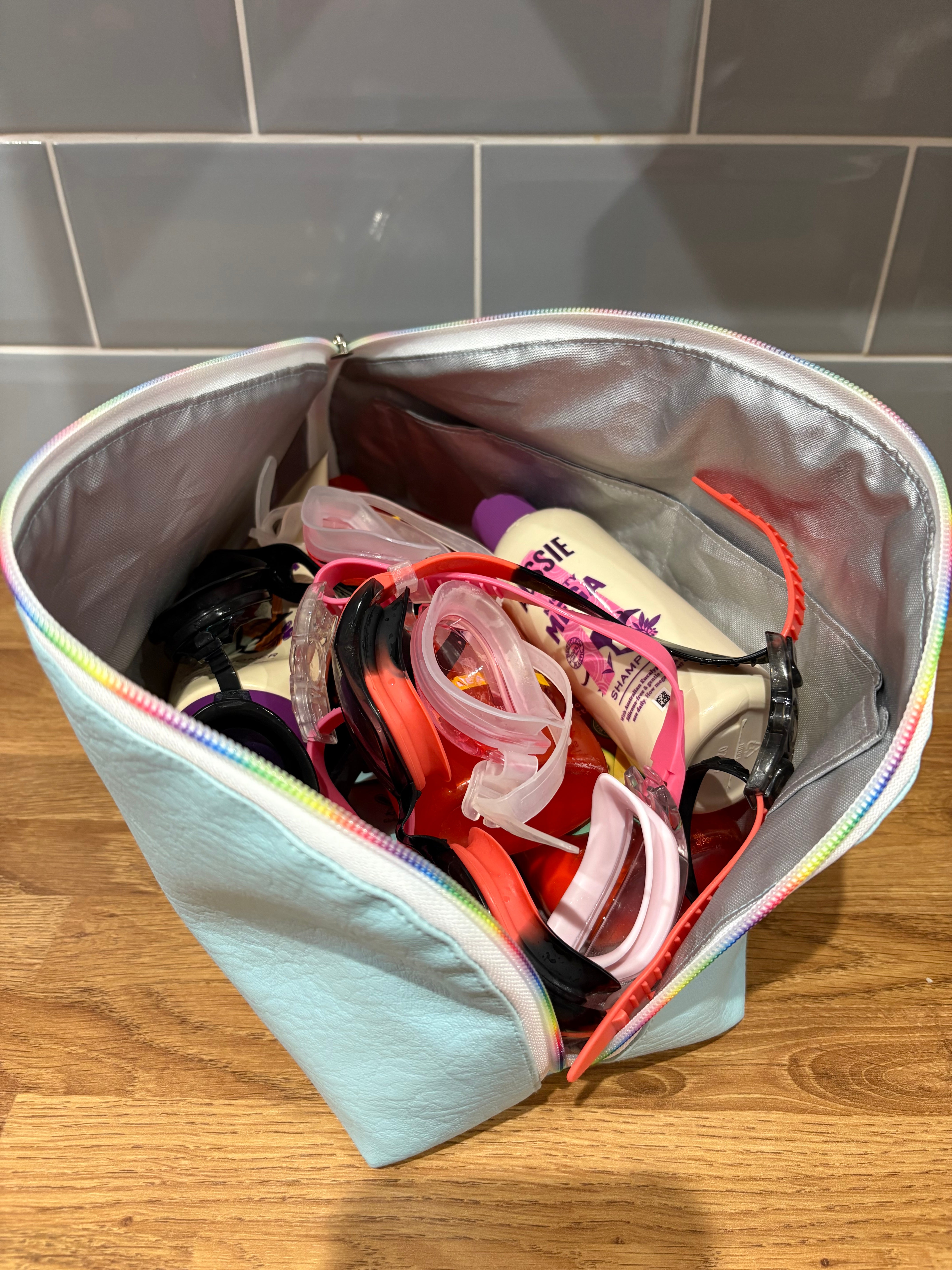 Multicolored bag with swimwear and bottles on a wooden floor.