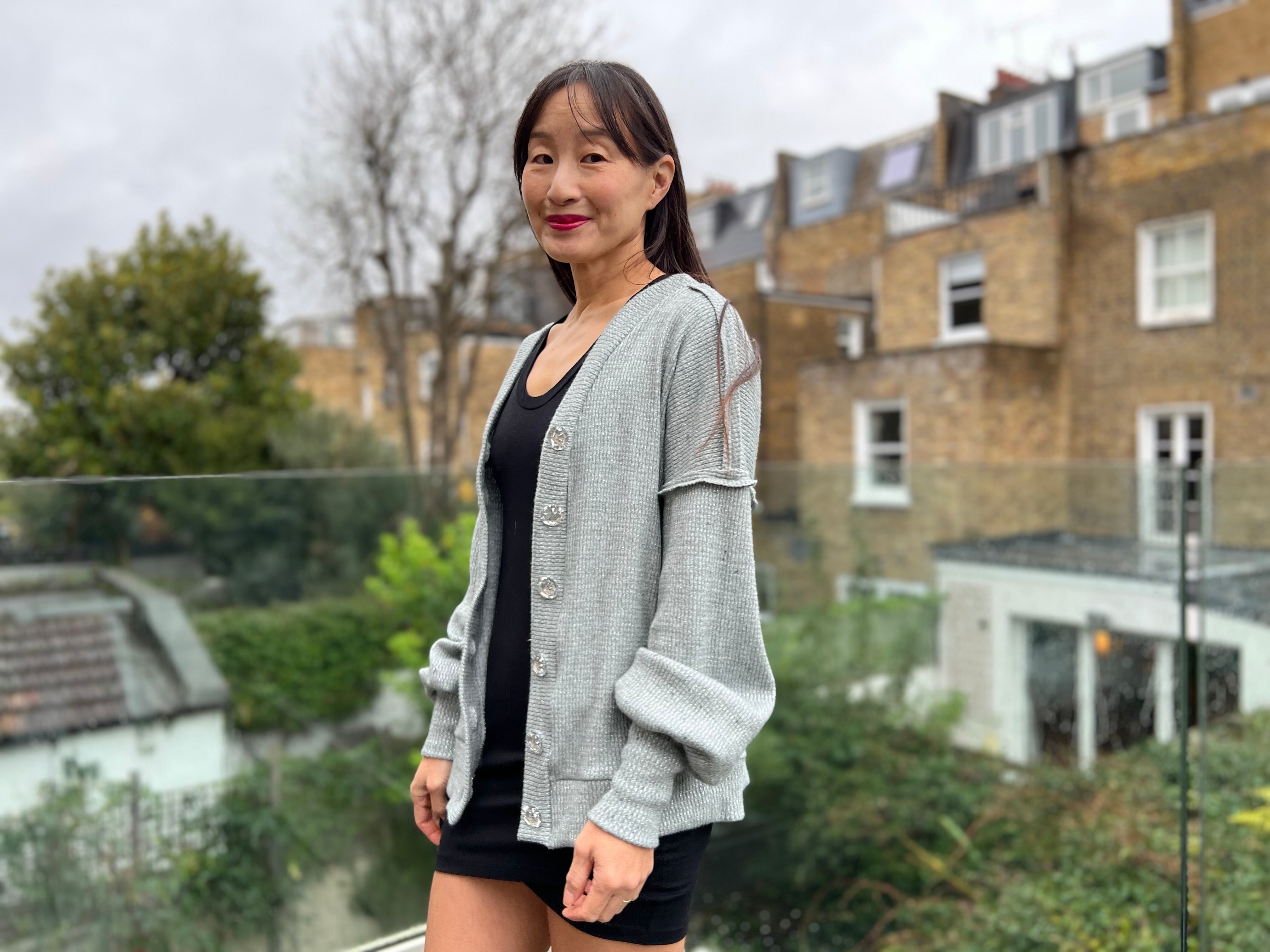 Woman wearing a black tulip dress with an oversized grey cardigan with bishop sleeves and tall cuffs. The seams are exposed on the shoulder.