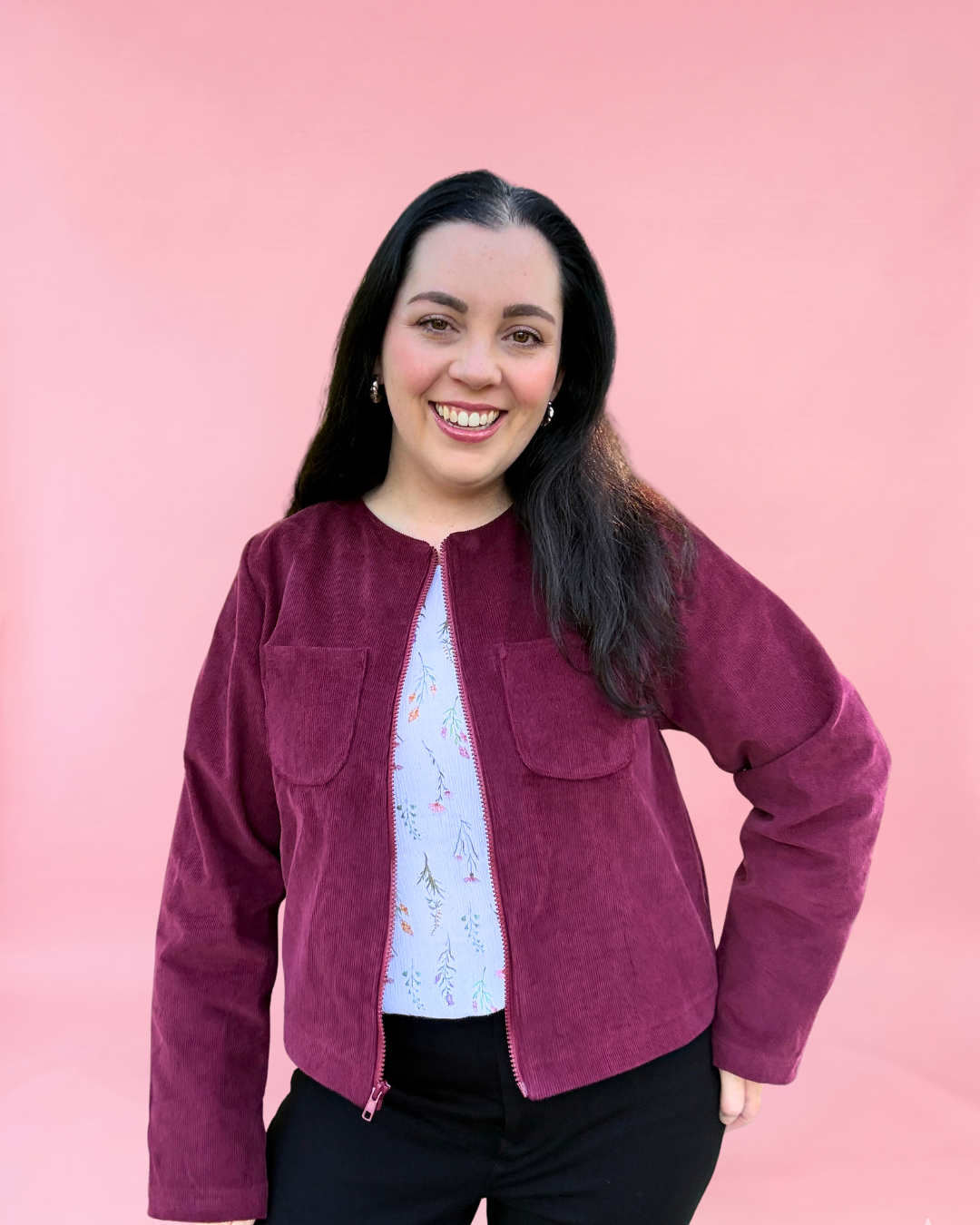 Woman wearing a maroon corduroy jacket against a pink background. Easy jacket sewing pattern with zipper.