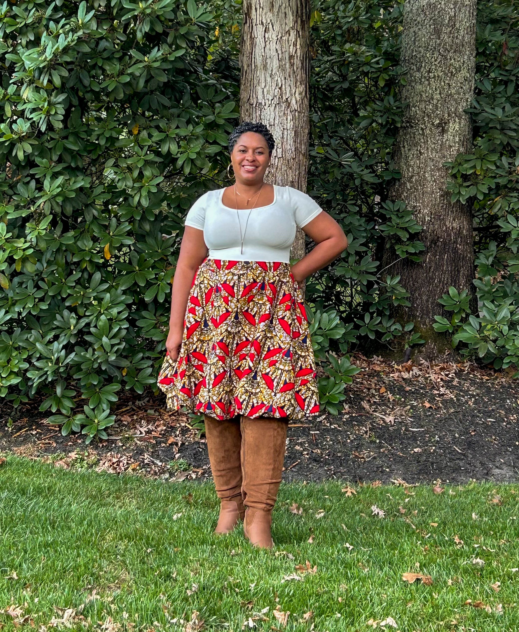 Woman standing outdoors in front of a tree, wearing a patterned, knee-length bubble skirt and brown suede knee boots.