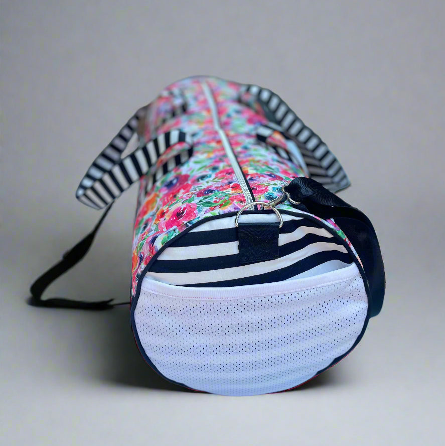 Serena Sports Duffle Bag in a waterproof floral canvas fabric and white and black contrasting bottom panel. Adjustable shoulder straps and hand straps. Side Zipper shoe compartment to keep dirty shoes away from clean clothes. Side mesh pocket for quick access to keys, phone, airpods, and more. Easy PDF sewing pattern by Ellie and Mac Sewing Patterns.