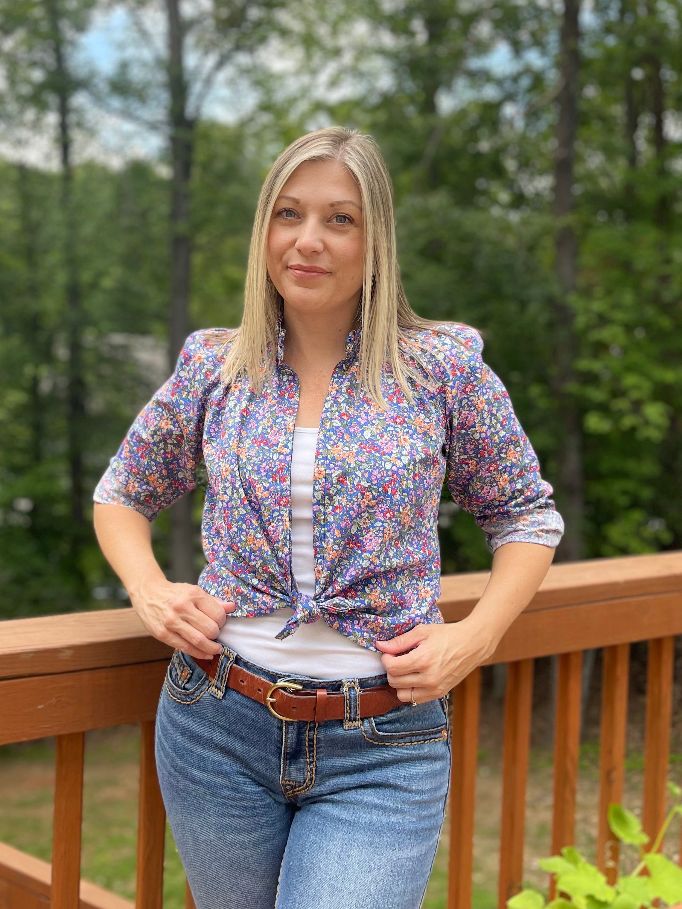 Button Down Hidden Placket Shirt Sewing Pattern by Ellie and Mac sewing patterns. This pattern is modeled on a blond woman with a white cami top and the floral woven button down top tied in front and the long sleeves rolled up 3/4.