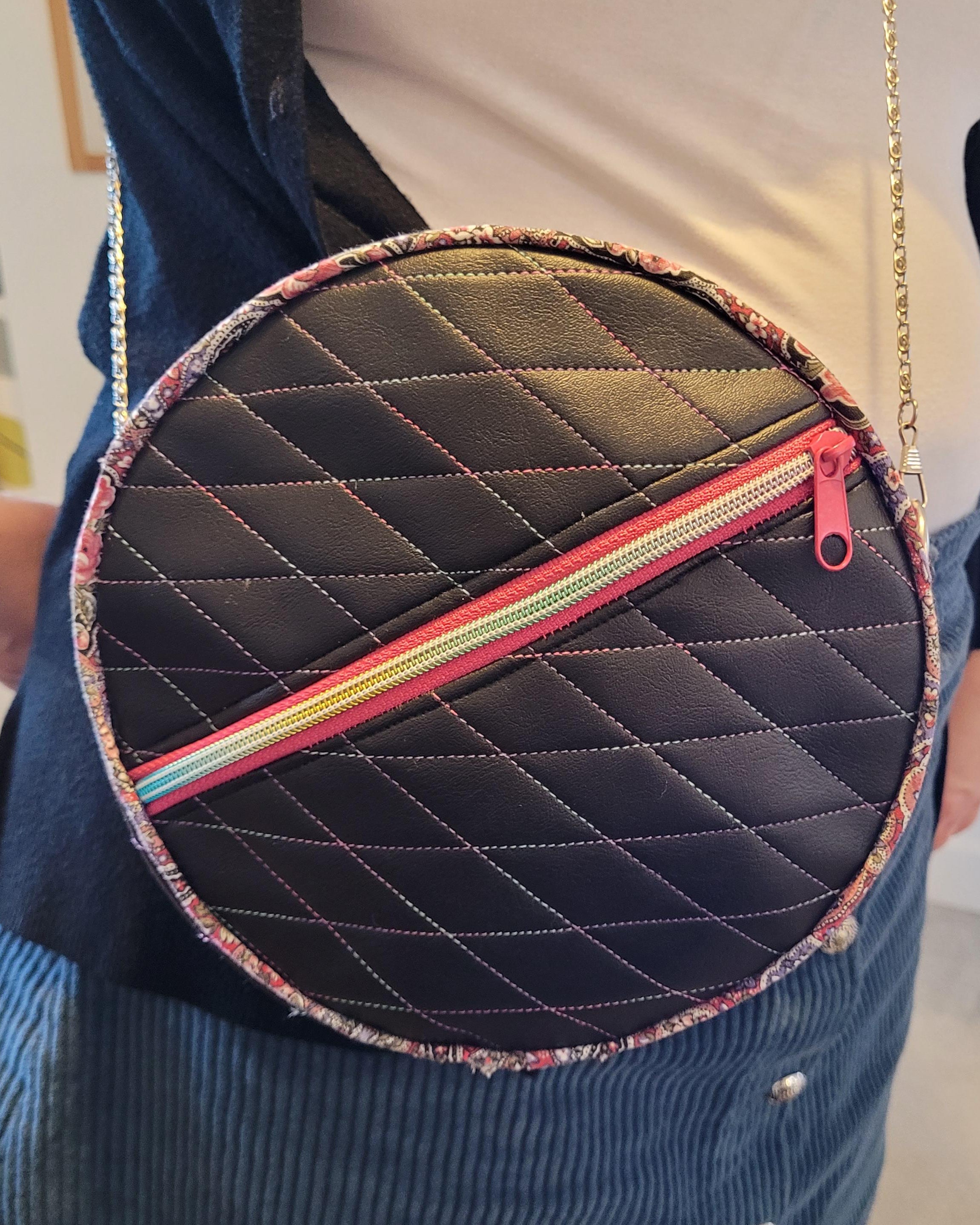 Round quilted bag with a zipper held by a person in a casual setting.