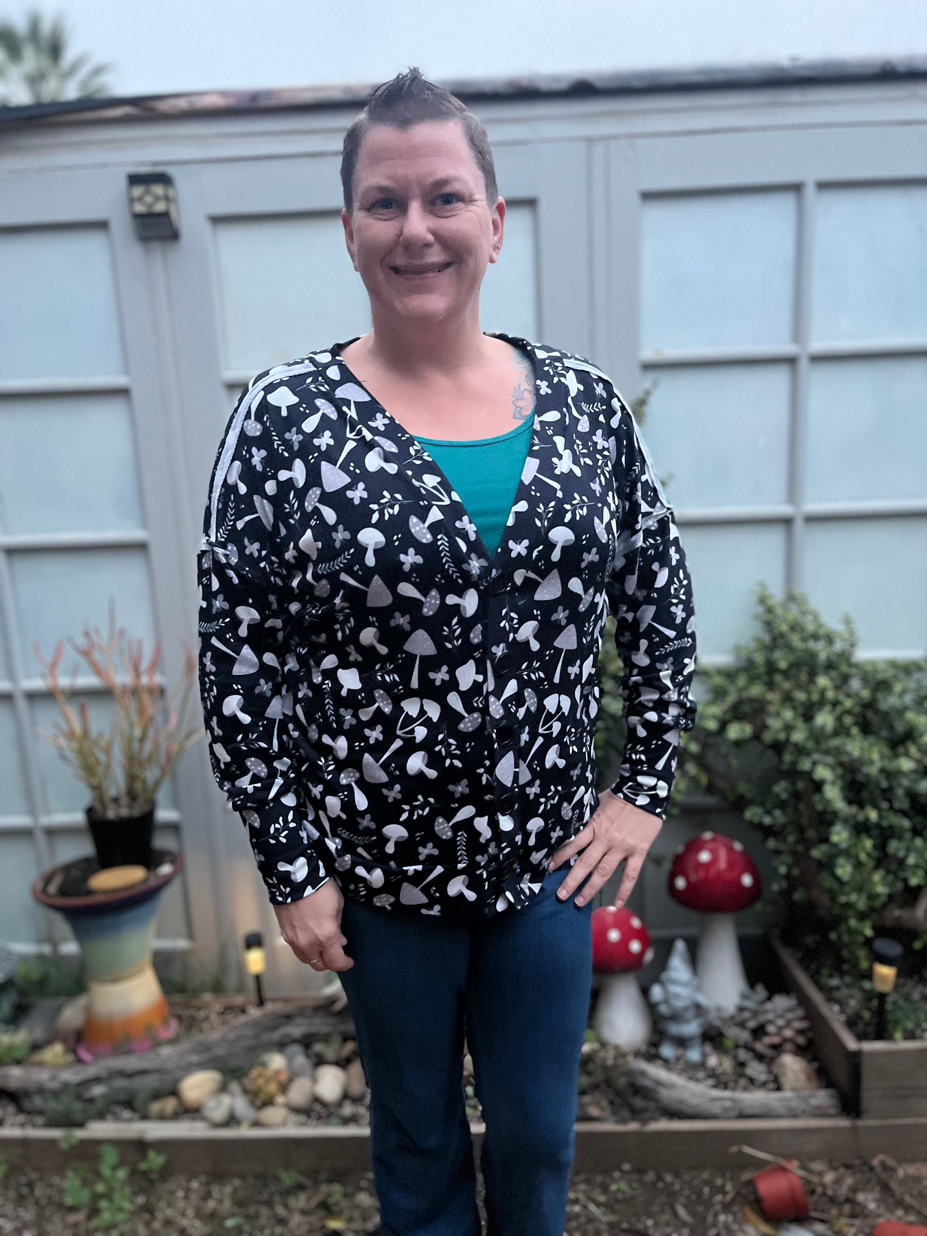 Woman wearing a black patterned cardigan over a teal shirt outdoors.