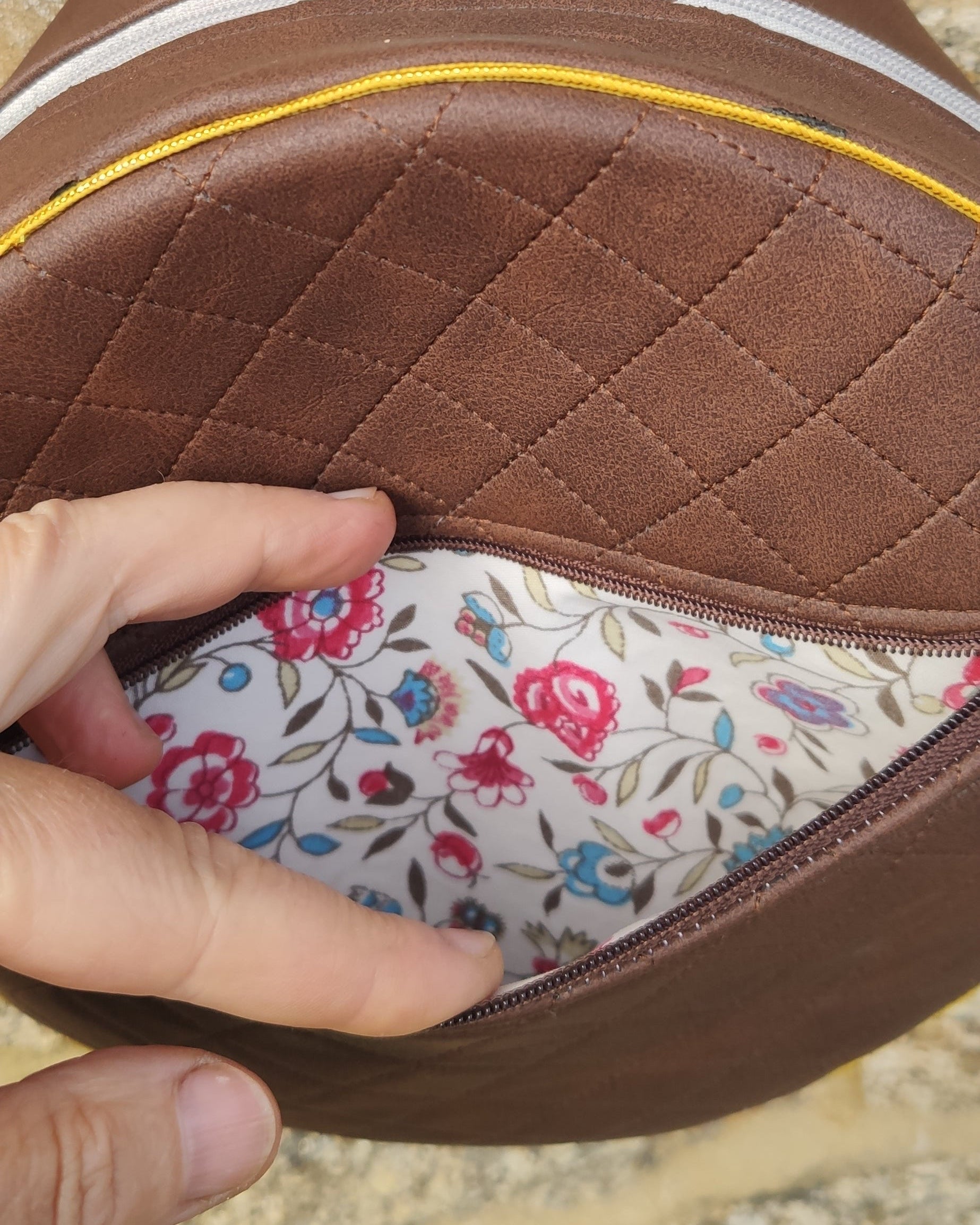 Close-up of a brown leather product with floral interior, held by a hand on a natural stone background.