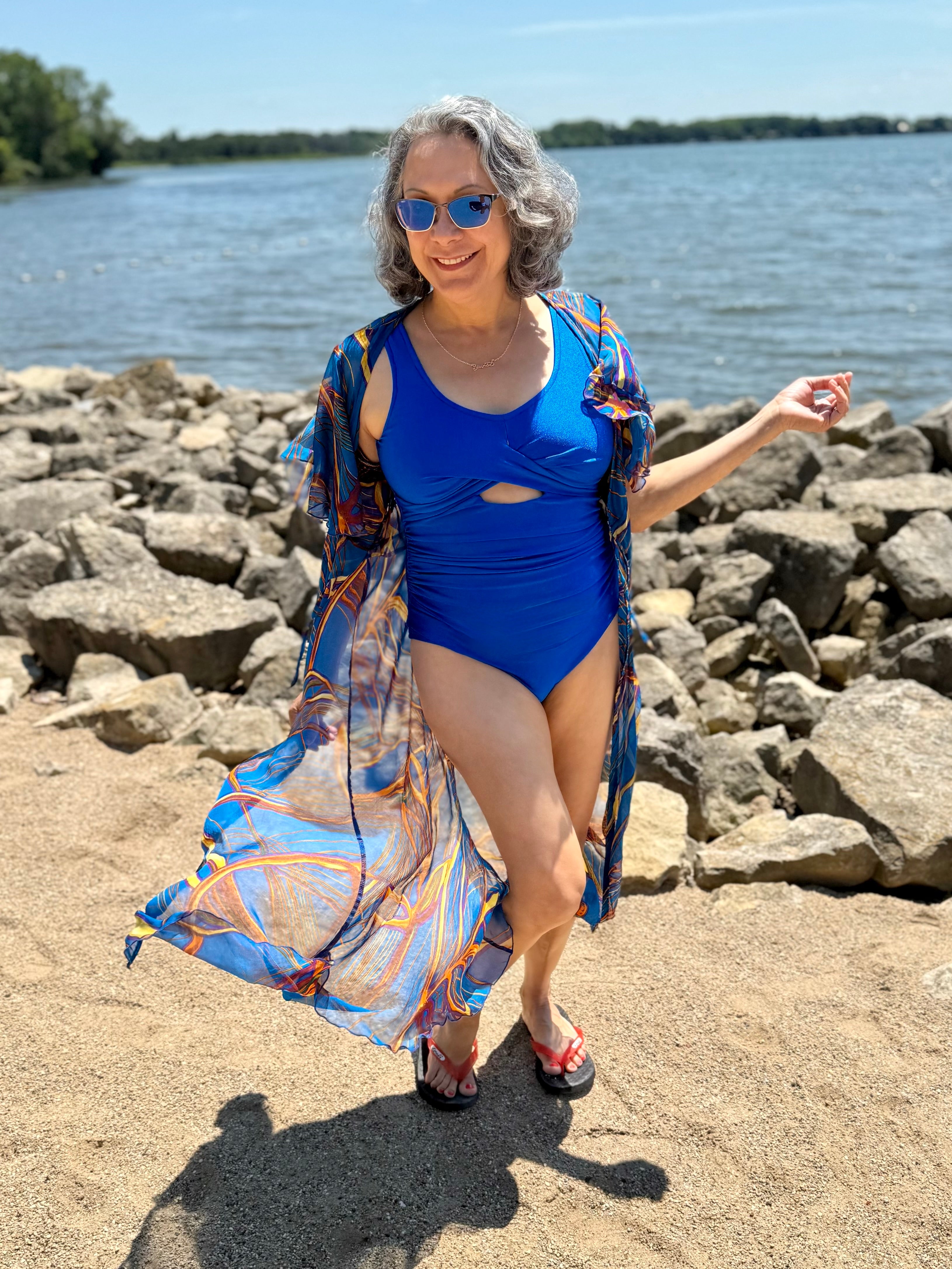 Woman in a blue swimsuit with a patterned cover-up standing on a rocky beach.