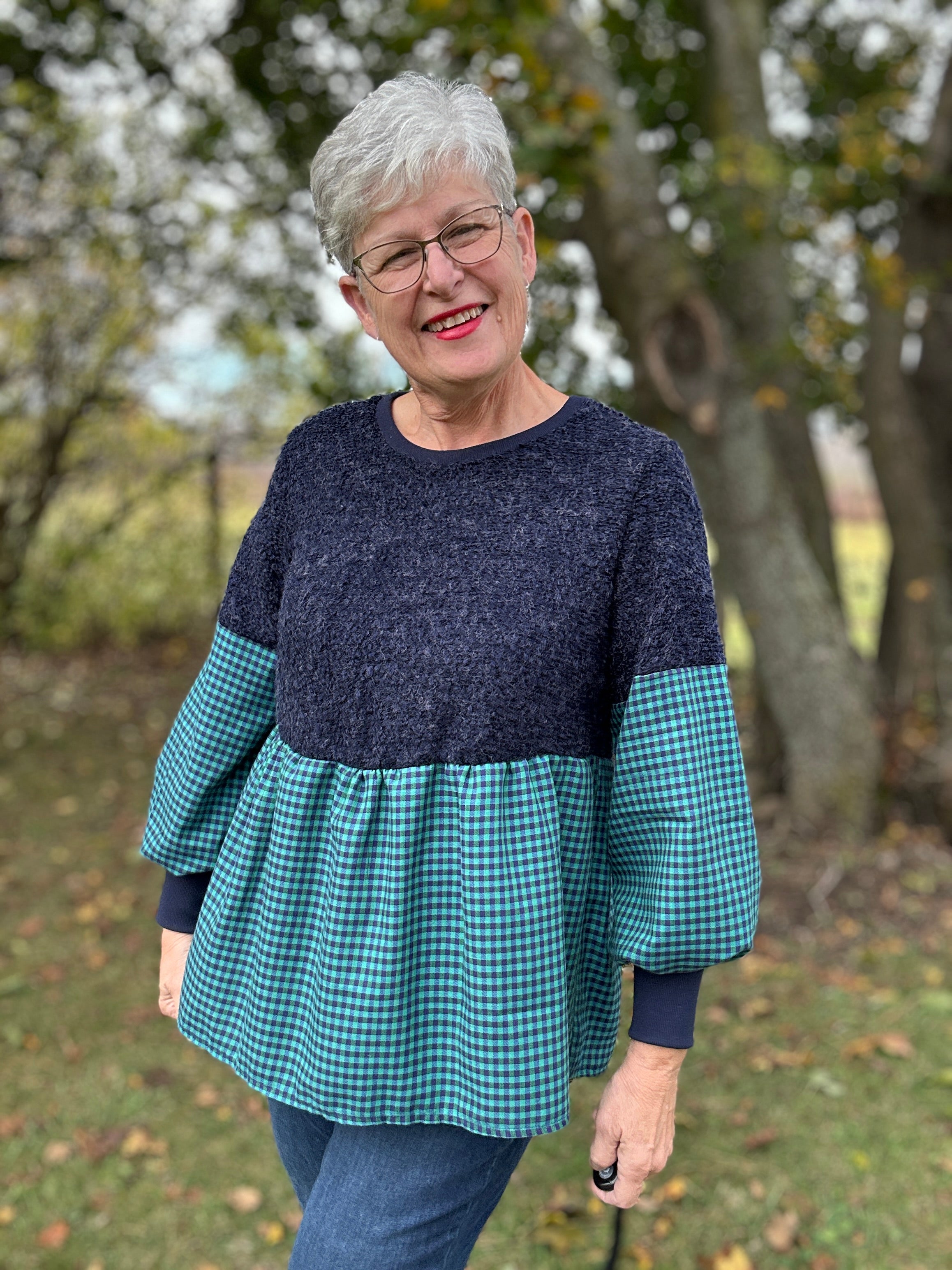 Woman wearing a blue and green checkered boho peasant top with a navy bodice in an outdoor setting.