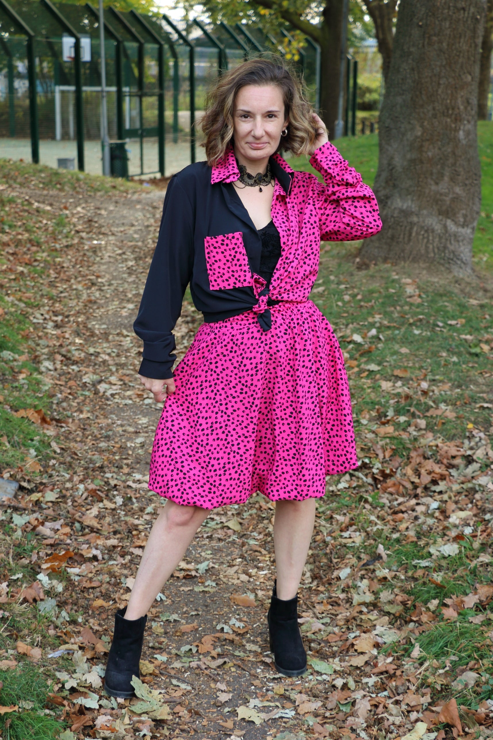 Woman wearing a black and pink outfit with a leopard print pattern in an outdoor setting. The shirt is made using the Connie Shacket pattern, The sweetheart top is made using the Nyeca pattern, and the skirt is made using the Sadie Bubble Skirt.
