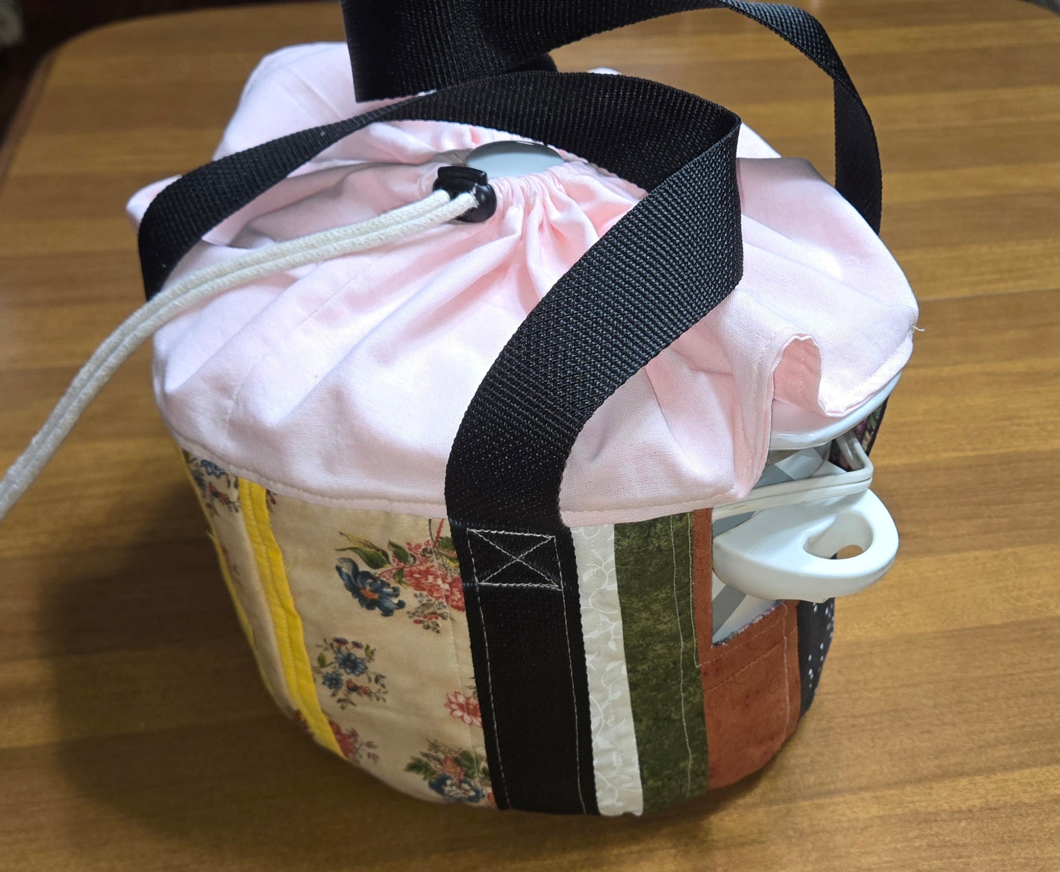 Fabric slow cooker carrier with floral pattern and black straps on a wooden surface.