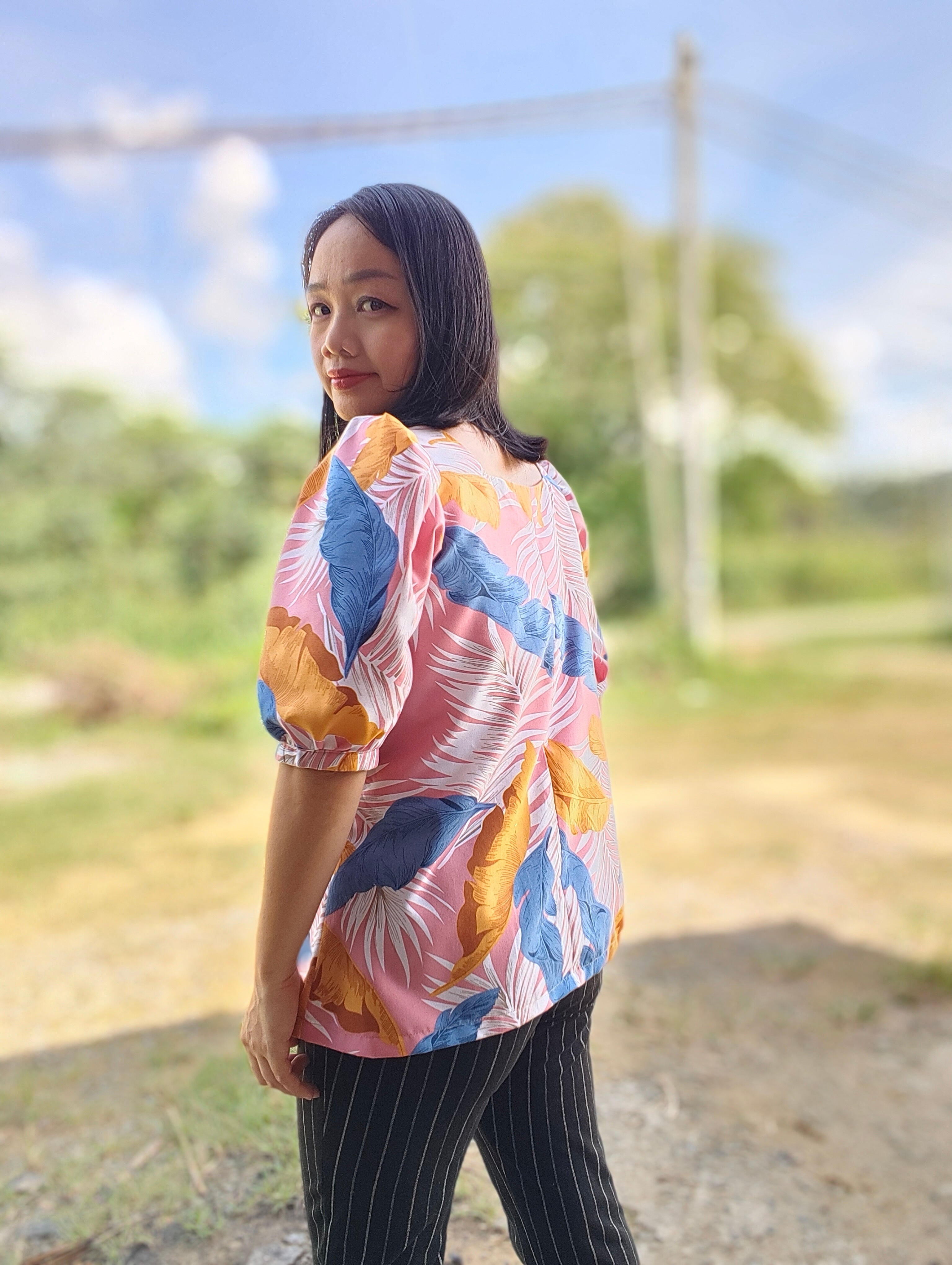Woman wearing a colorful patterned shirt outdoors with trees and power lines in the background
