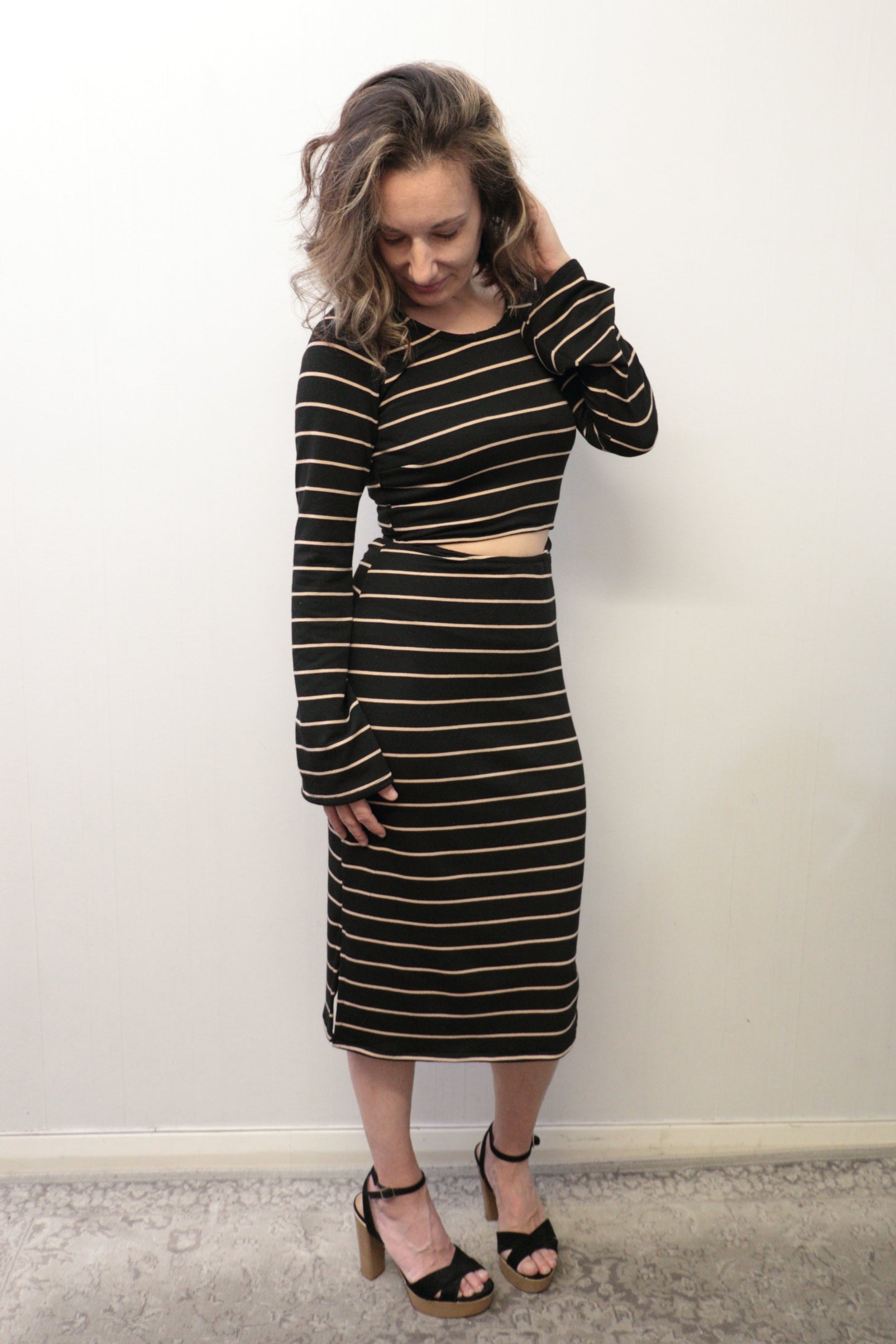 Woman wearing a black and gold striped dress against a white wall. Bell sleeve and front and back cutouts make this dress a must-have. PDF sewing pattern