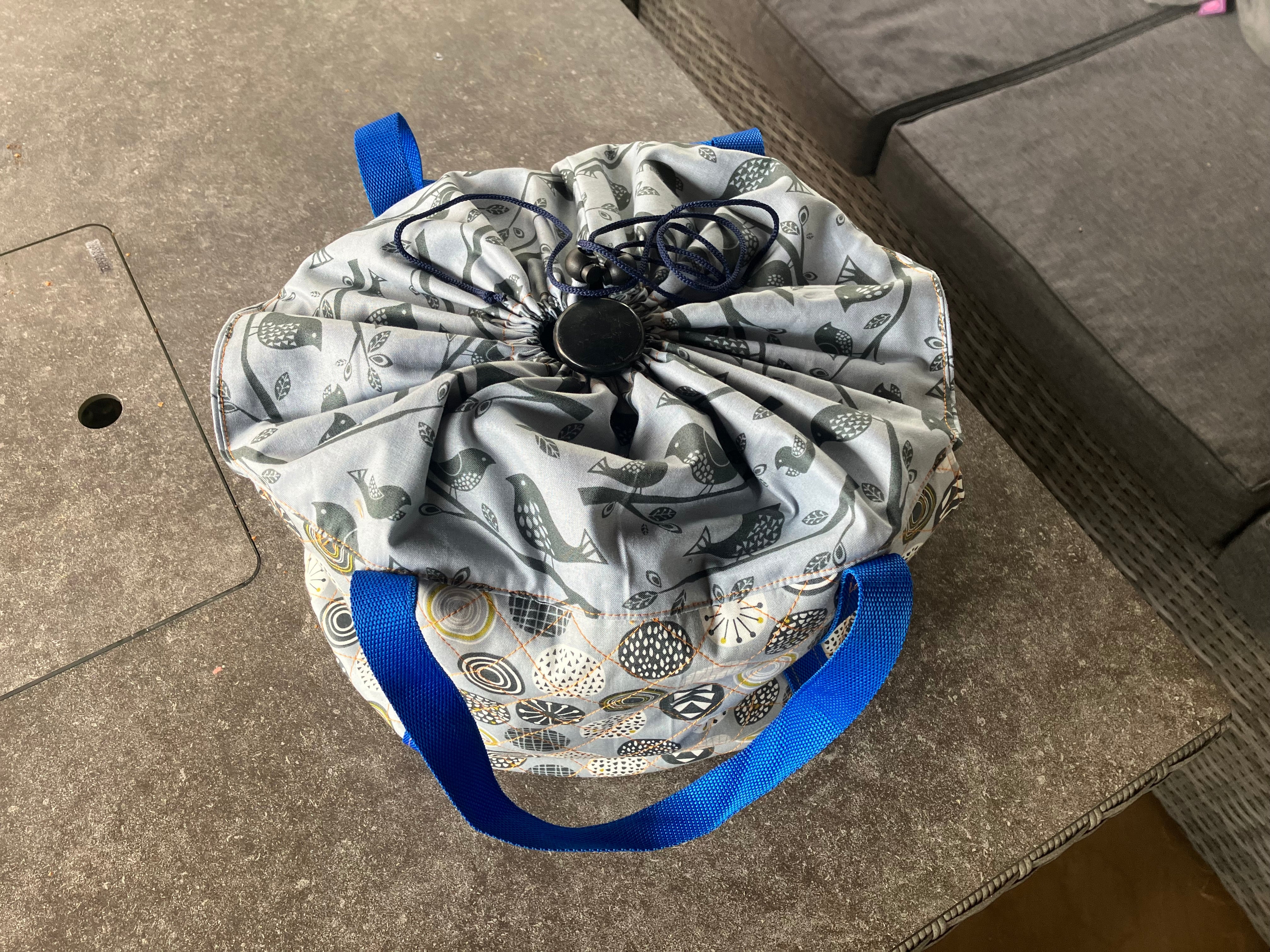 Drawstring top of the slow cooker bag with blue straps on a concrete surface. This carrier was made using the warm and cozy slow cooker carrier pattern by Ellie and Mac sewing patterns.