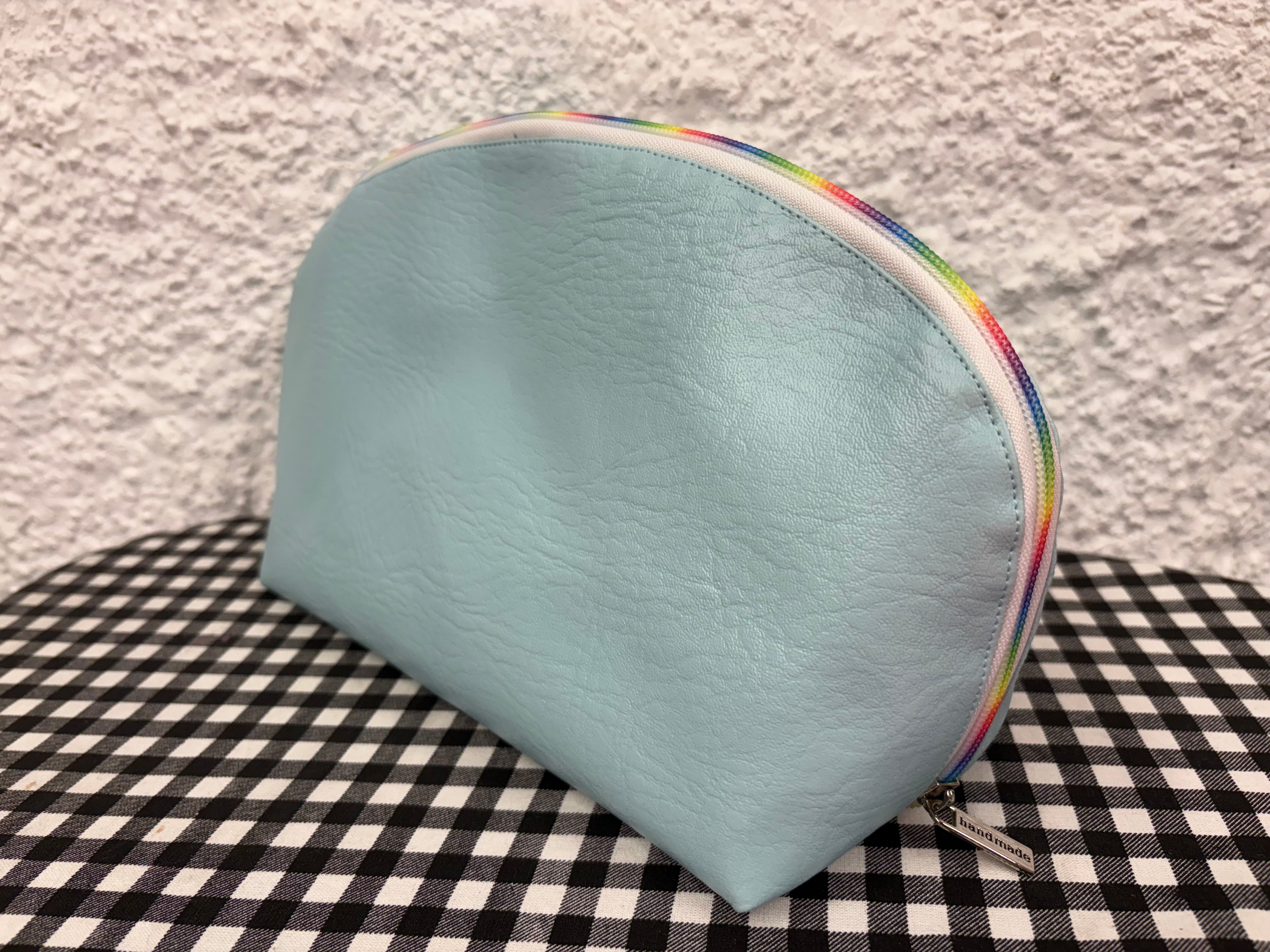 Light blue pouch with rainbow zipper on a checkered fabric background. Fabric texture and clean stitching on the Tessa zipper pouch sewing pattern.