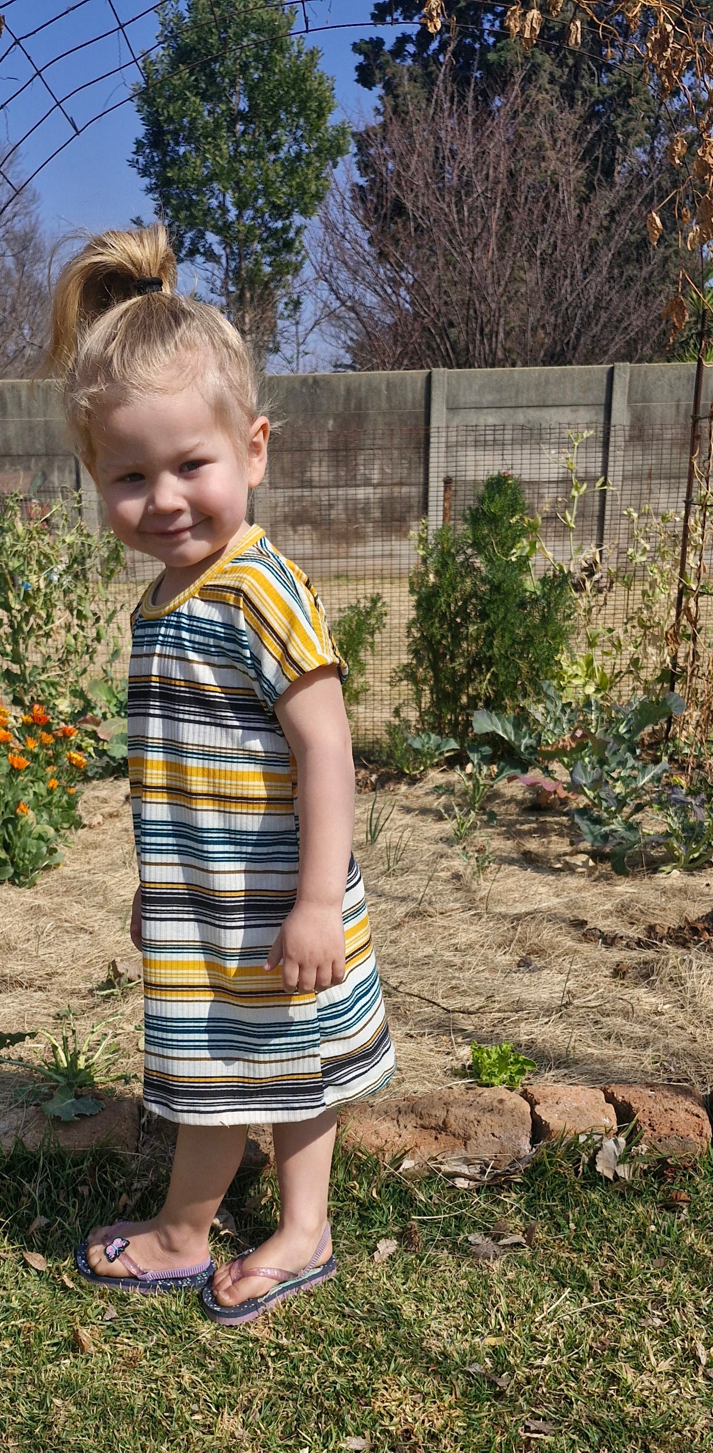 Child wearing a striped dress standing in a garden
