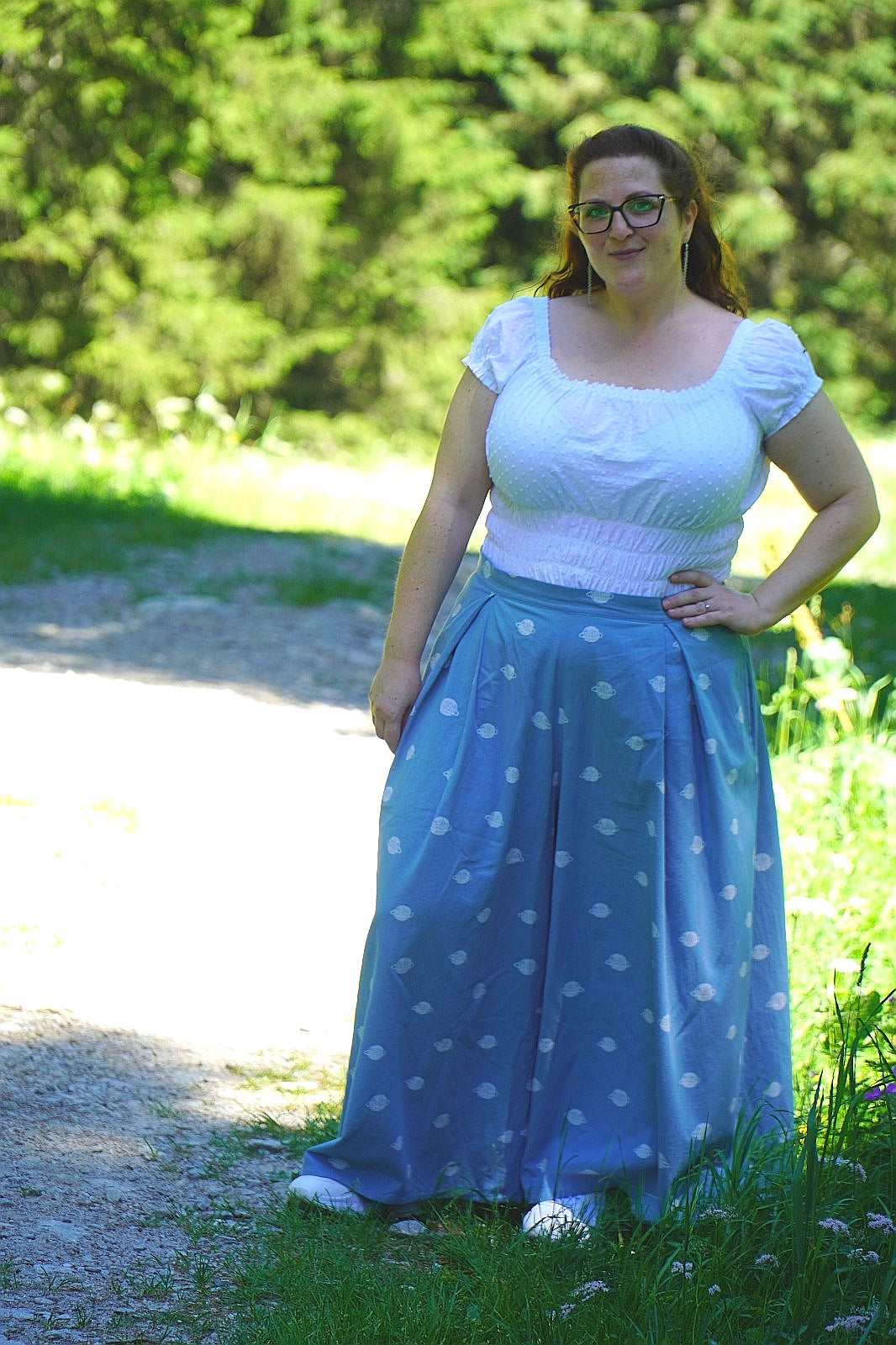 Woman wearing a white shirred top with cap sleeves and square neckline and blue polka dot skirt standing outdoors with greenery in the background. Sewn with Ellie and Mac digital sewing patterns. #1 sewing patterns.