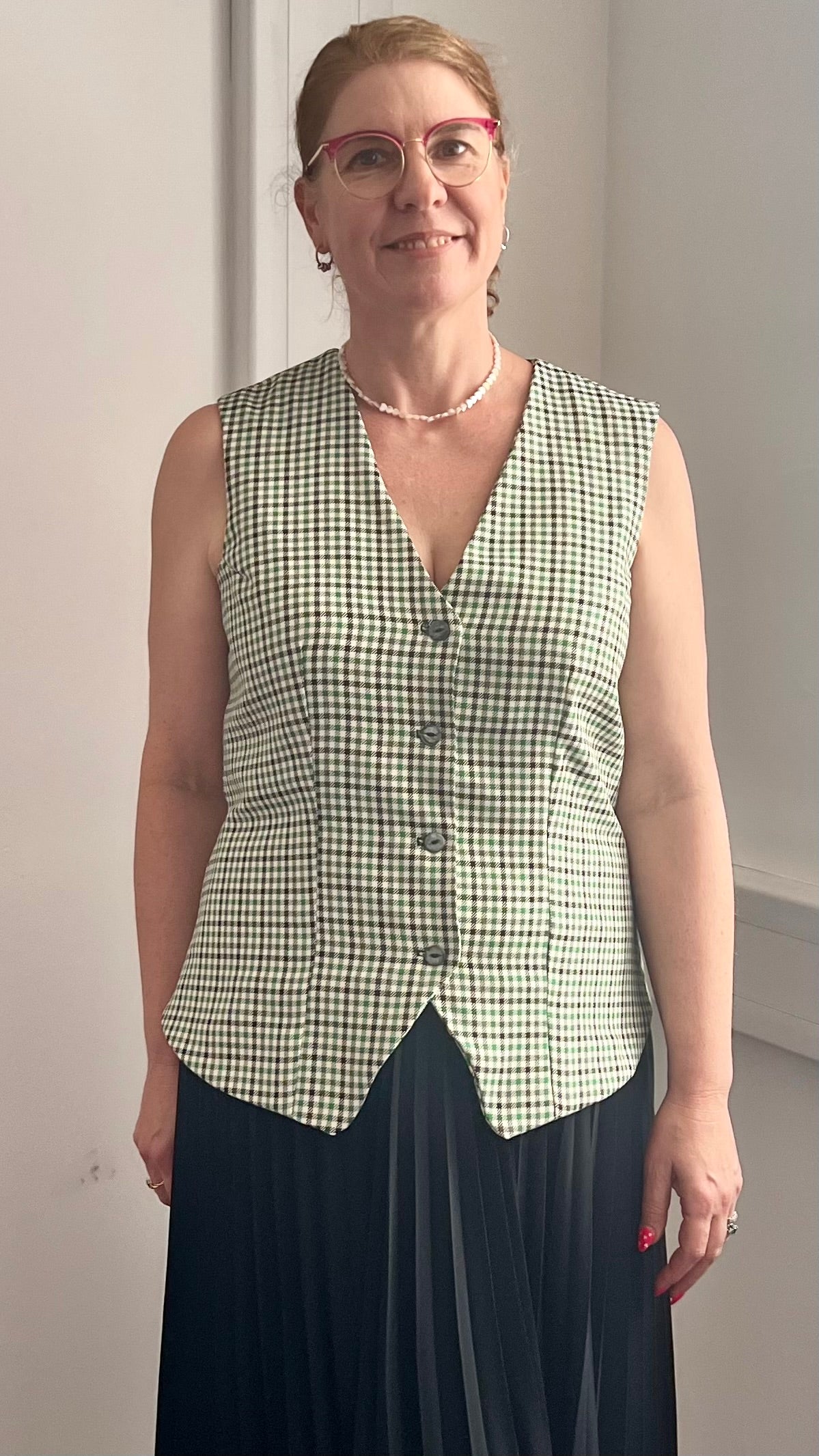 Woman wearing a green checkered vest over a black dress against a plain background