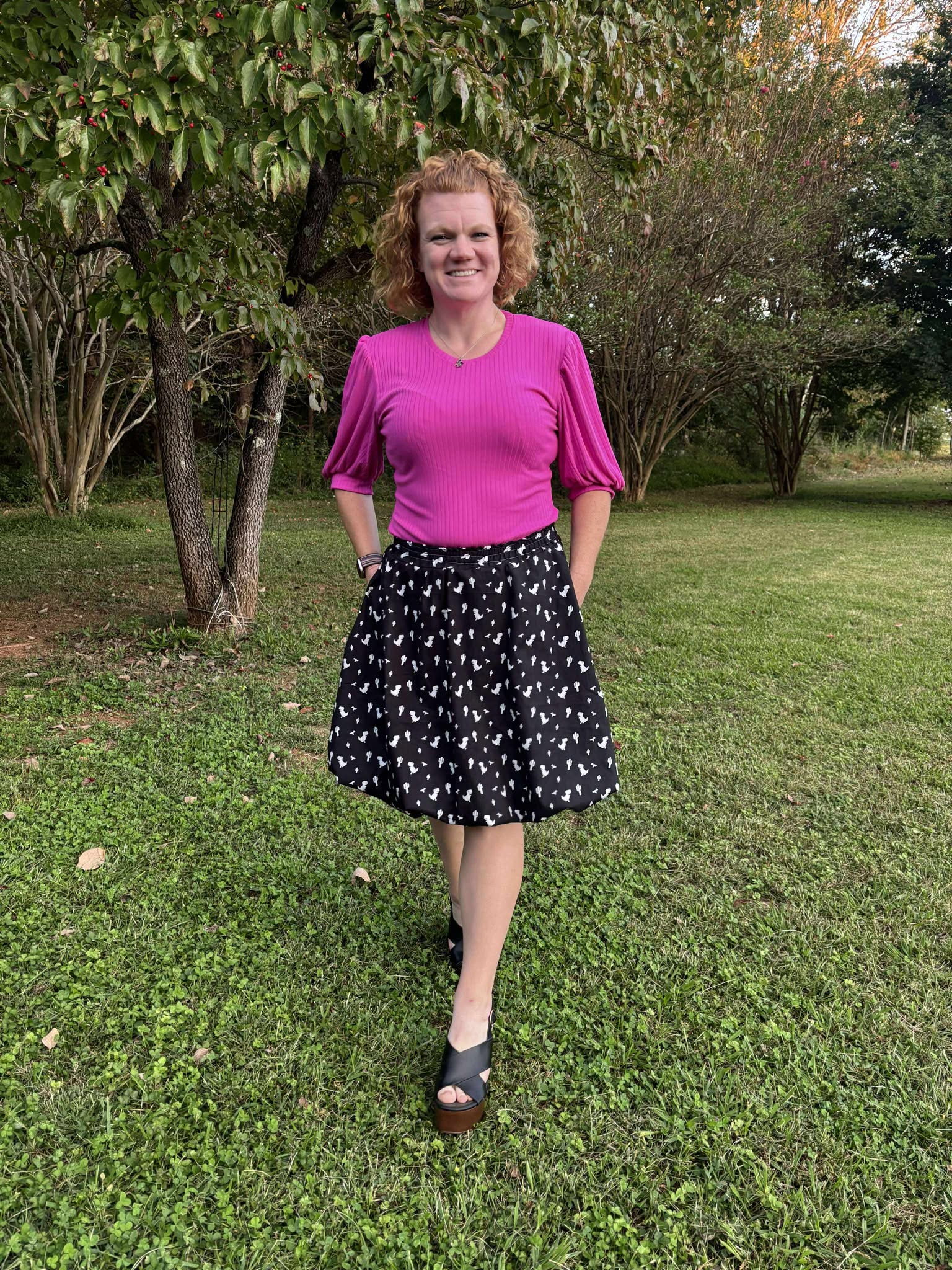 Woman wearing a pink top and black skirt with white patterns outdoors.