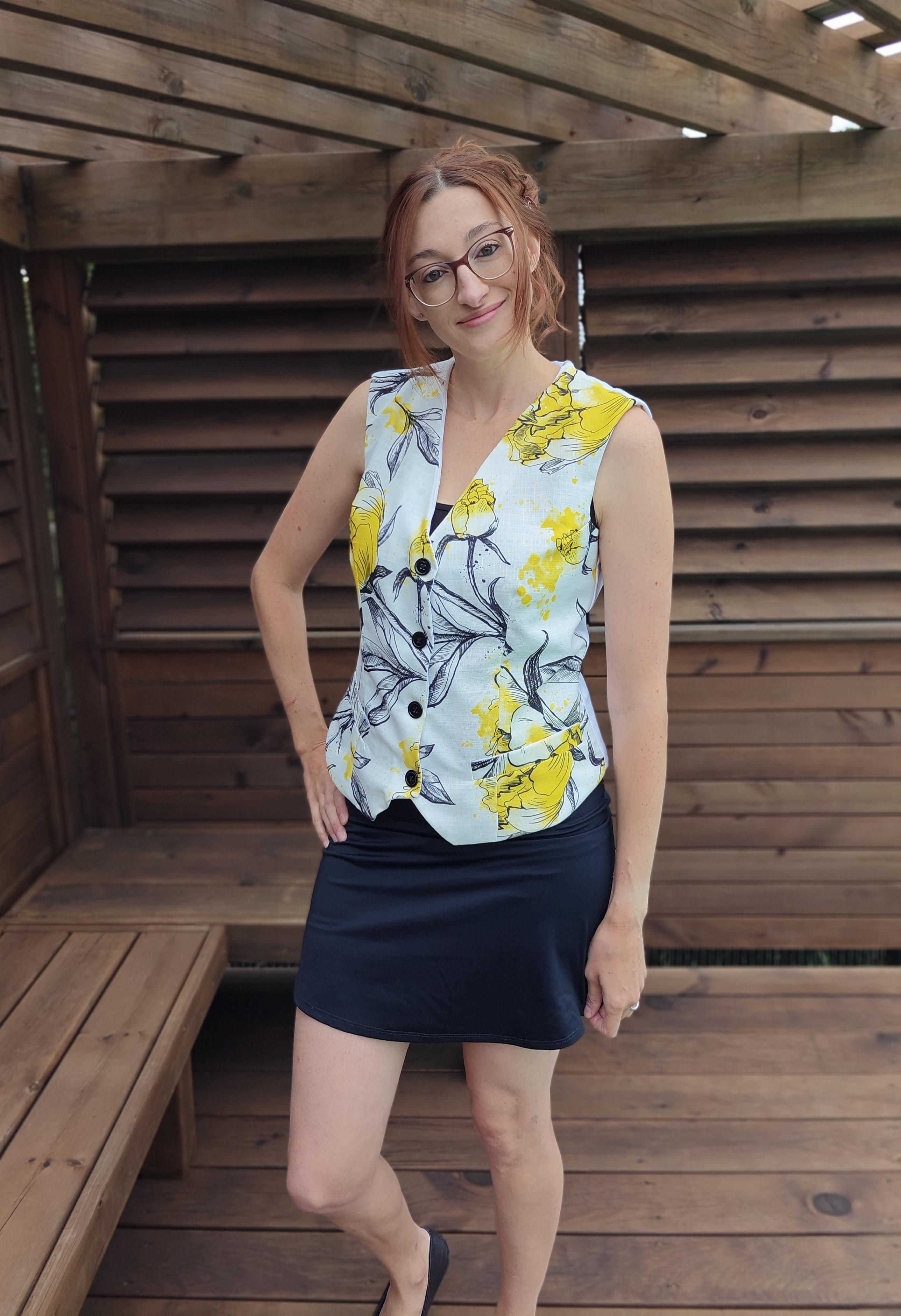 Woman wearing a floral waistcoat and black skirt standing in a wooden structure.