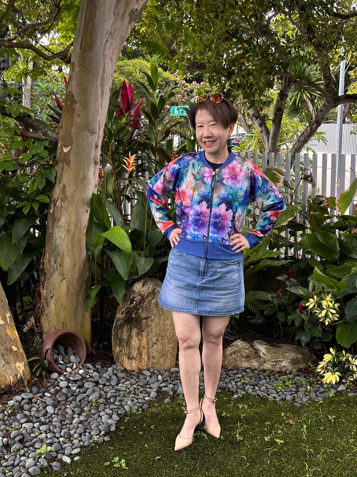 Woman outside modeling a floral and blue athletic bomber jacket with zip closure, kangaroo pocket detail, and cuffs. Easy pdf sewing pattern.