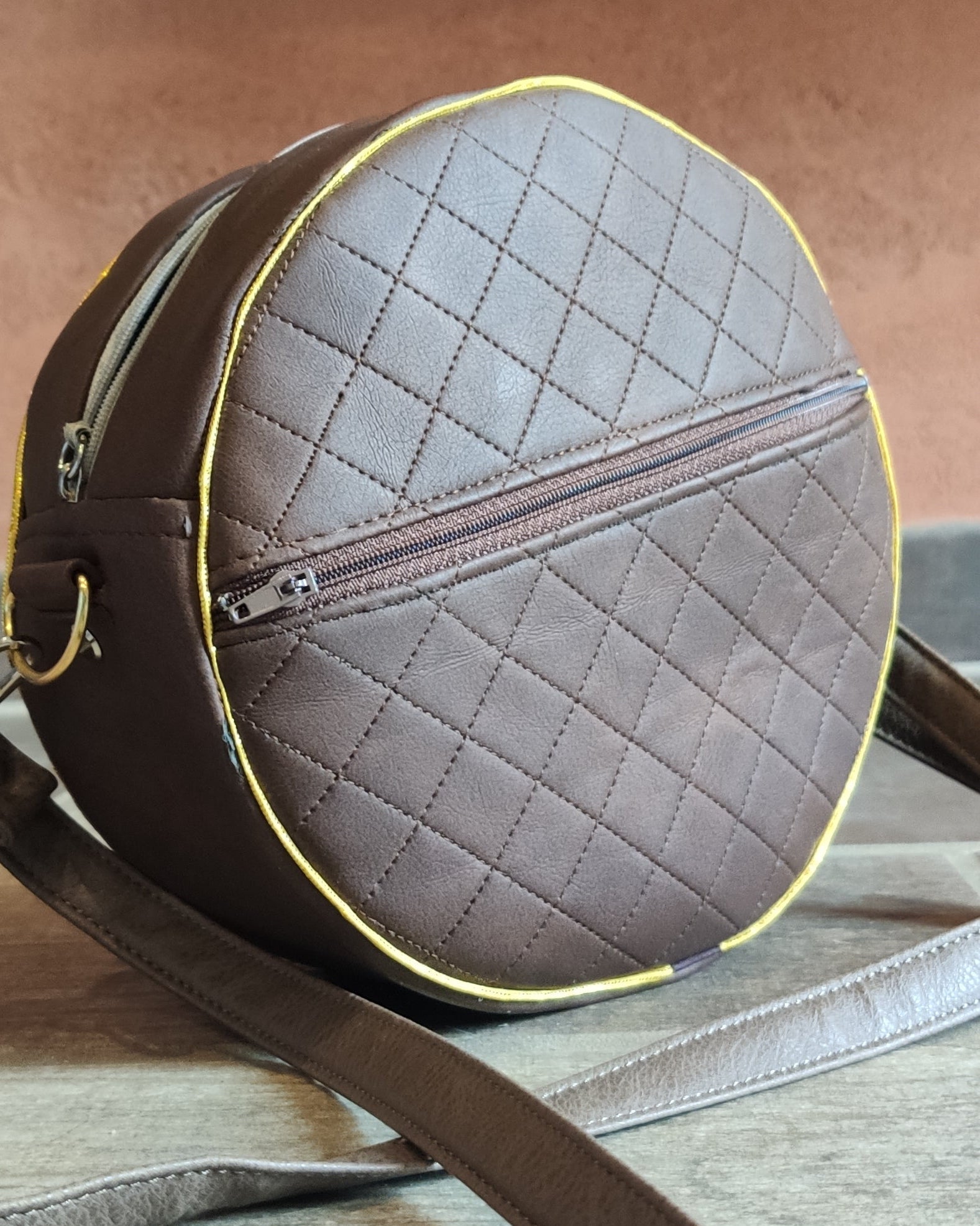 Round quilted leather bag with a strap on a wooden surface