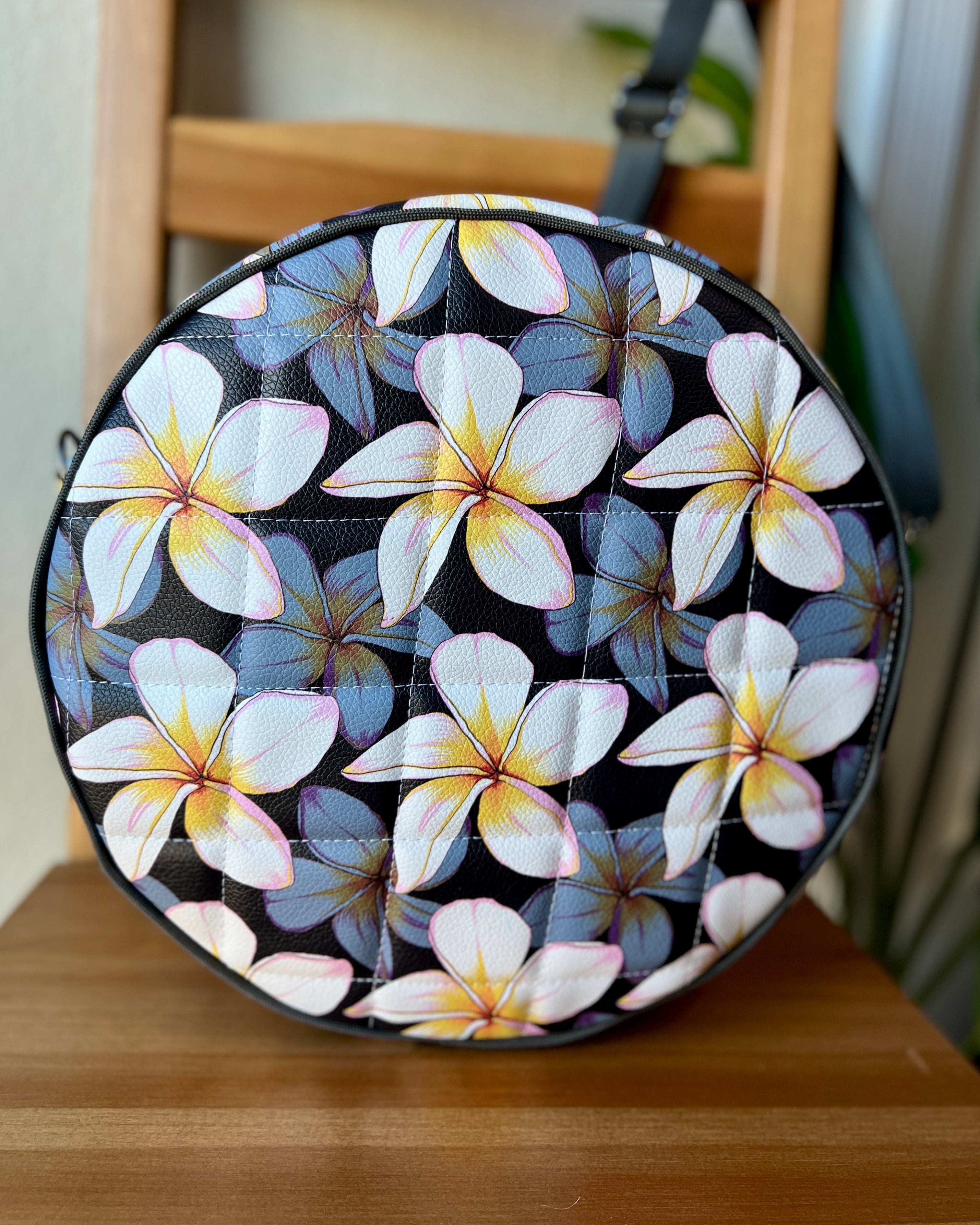 Handcrafted round vinyl bag in black floral vinyl with black hardware and hidden strap connectors.