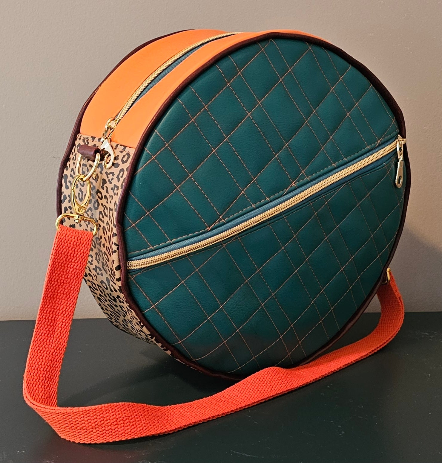 Teal handmade round bag with orange strap and leopard print accents on a dark surface.