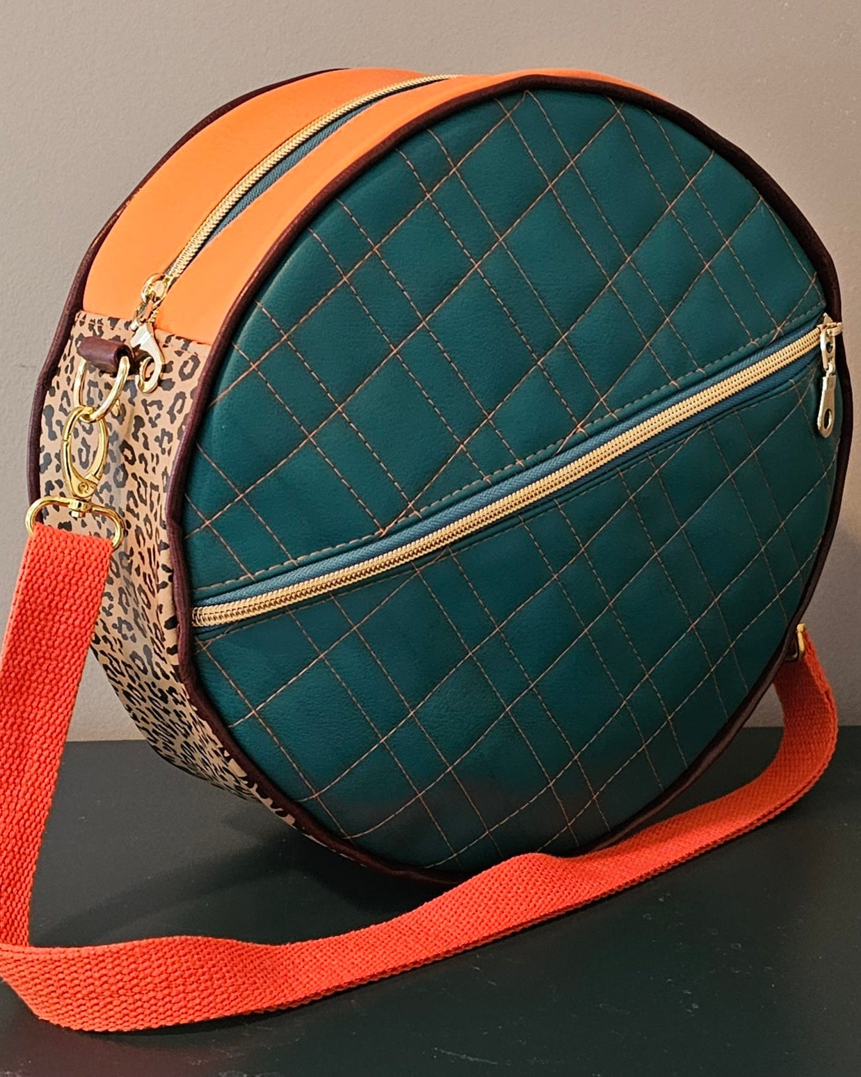 Teal handmade round bag with orange strap and leopard print accents on a dark surface.