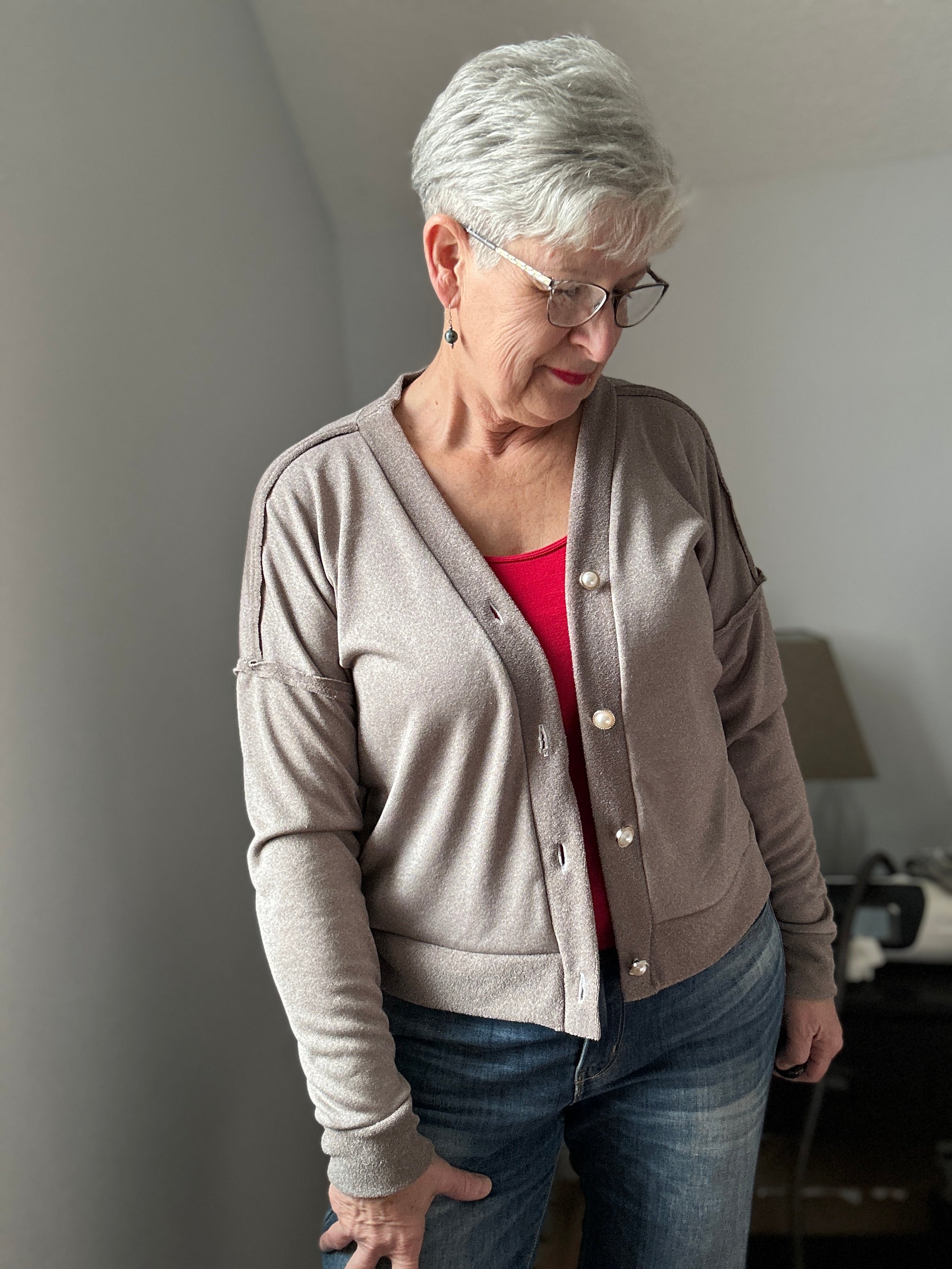 Woman wearing a beige cardigan over a red shirt, standing indoors.