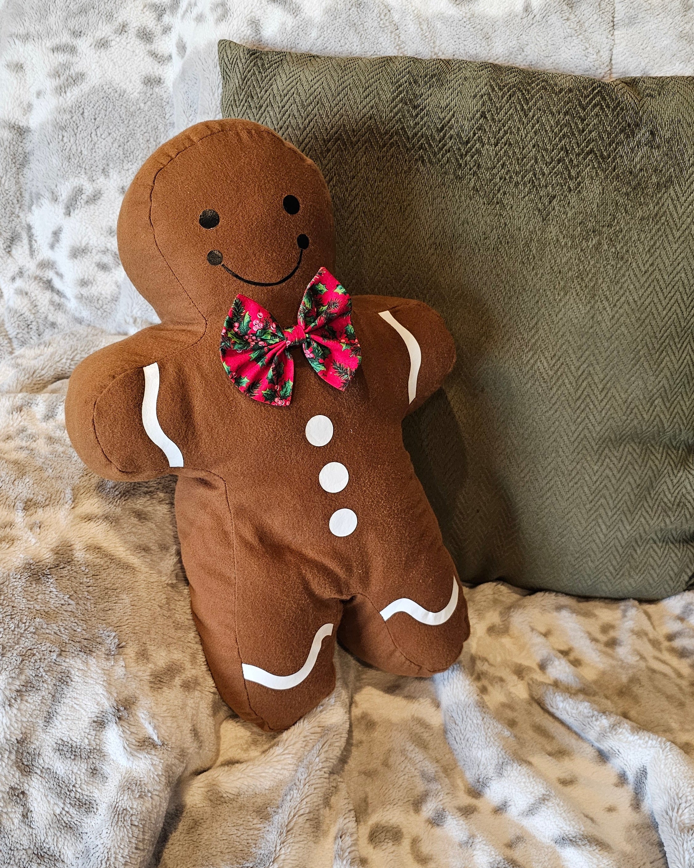 Gingerbread man plush toy with a smiling face, bow tie, and buttons on a textured surface
