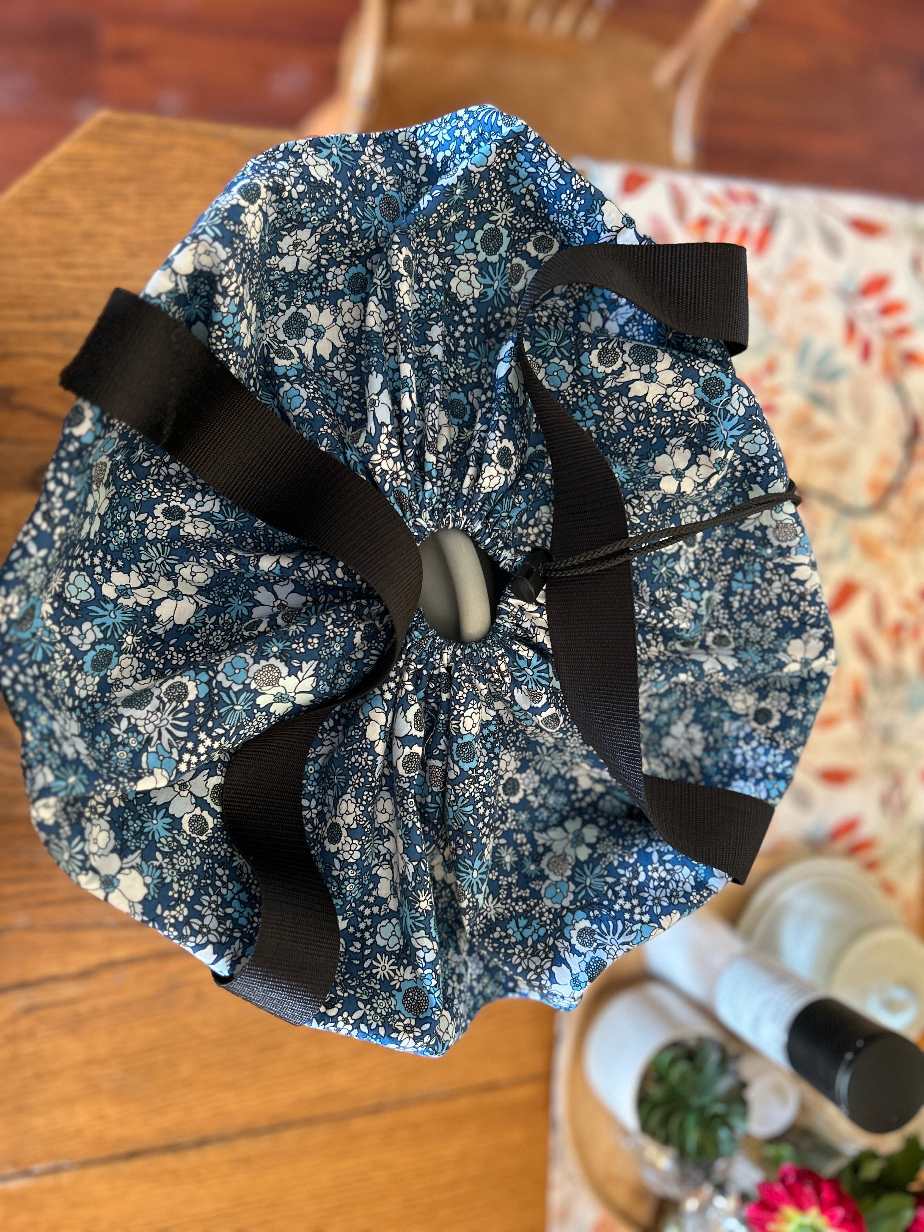 Top view of the blue floral fabric slow cooker carrier with black ribbon on a wooden surface. This carrier was made using the warm and cozy slow cooker carrier pattern by Ellie and Mac sewing patterns.