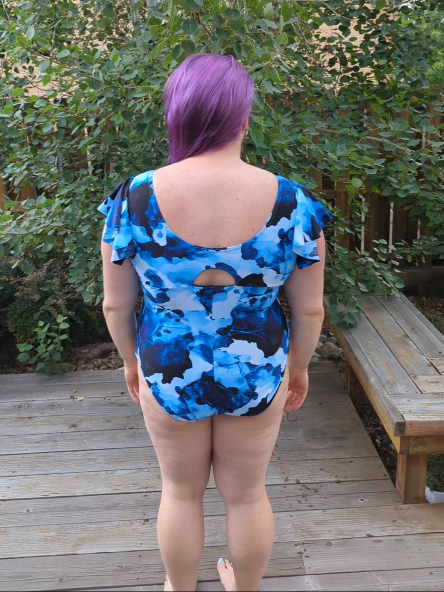 Person wearing a blue camouflage swimsuit standing outdoors on a wooden deck with greenery in the background.