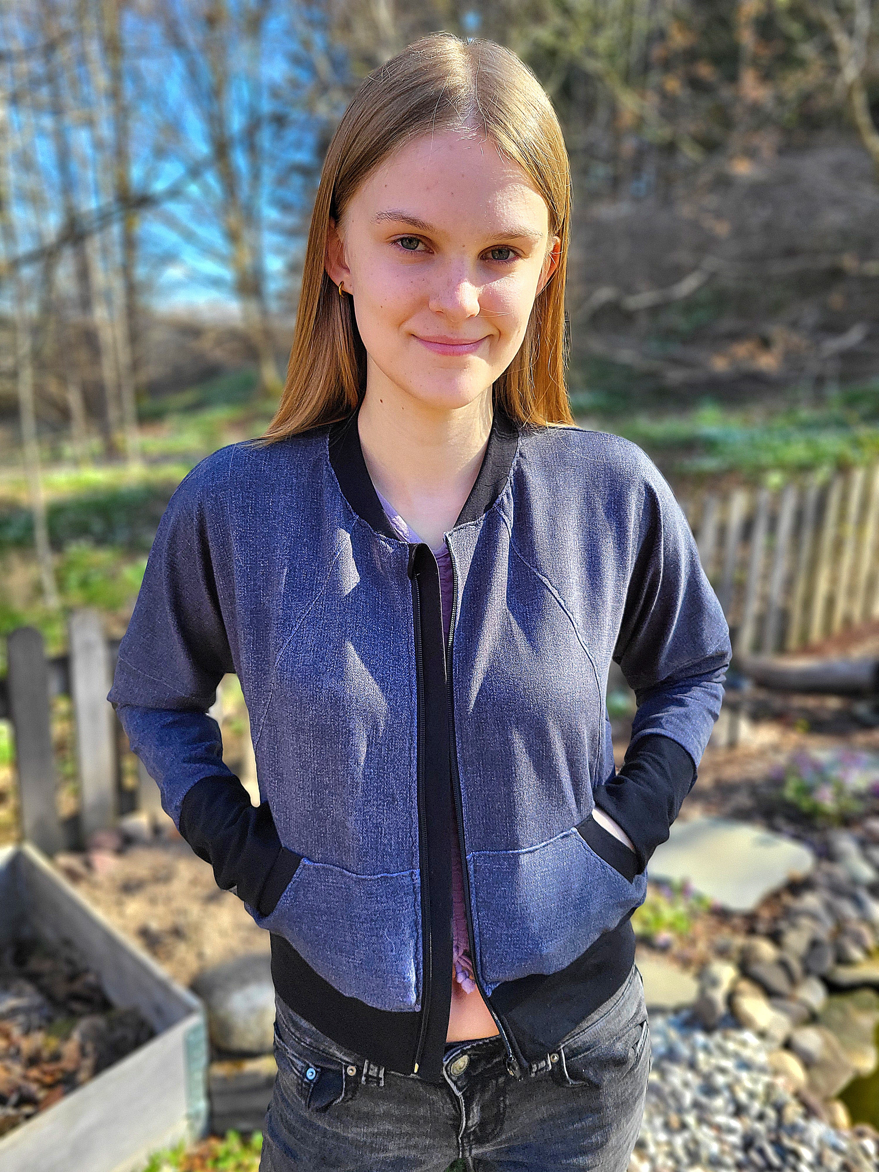 Teen girl wearing a denim knit fabric zip-up bomber jacket with raglan dolman sleeves, kangaroo pocket, and curved waistband. Knit fabric sewing pattern - instant download.