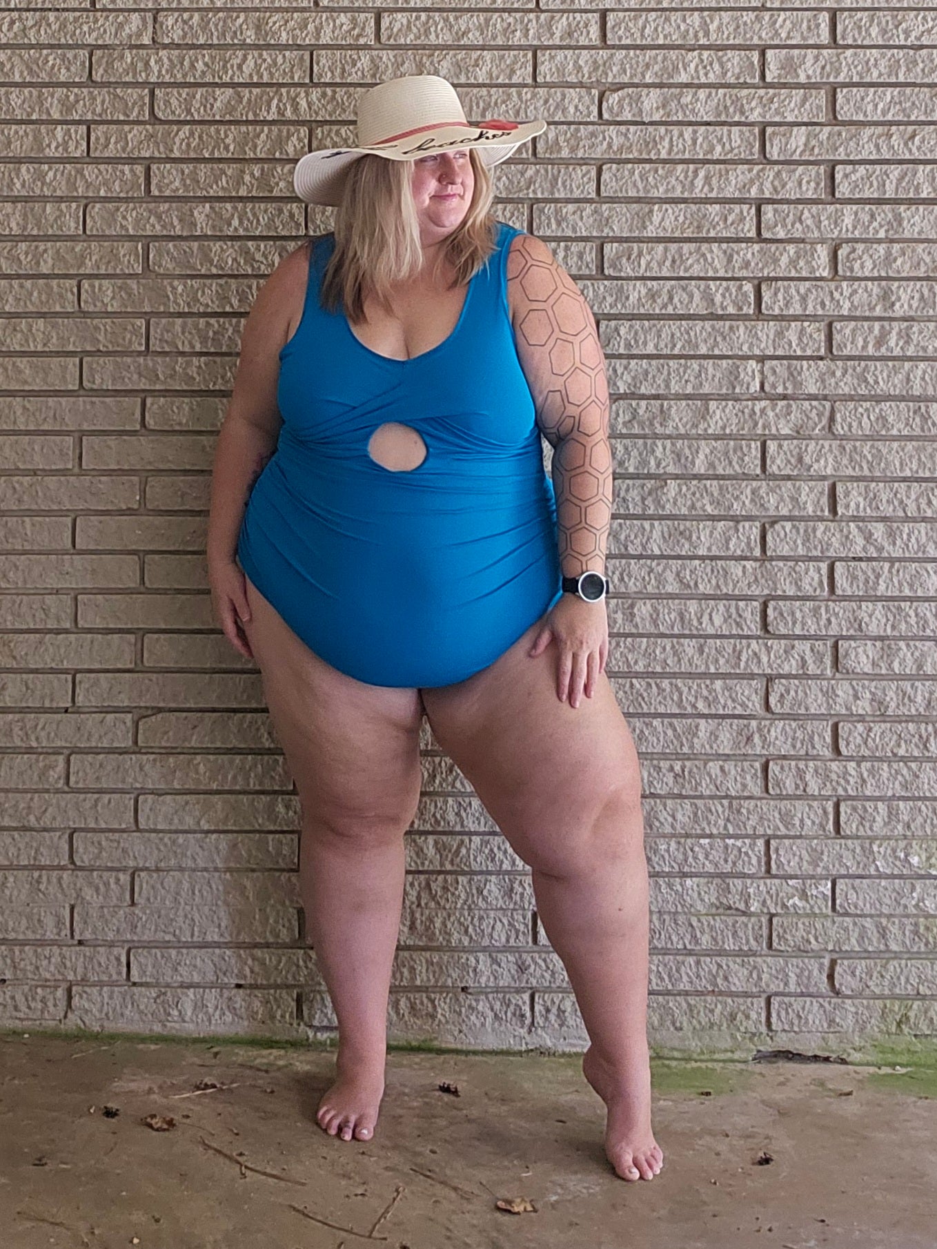 Person wearing a blue swimsuit and straw hat against a brick wall.