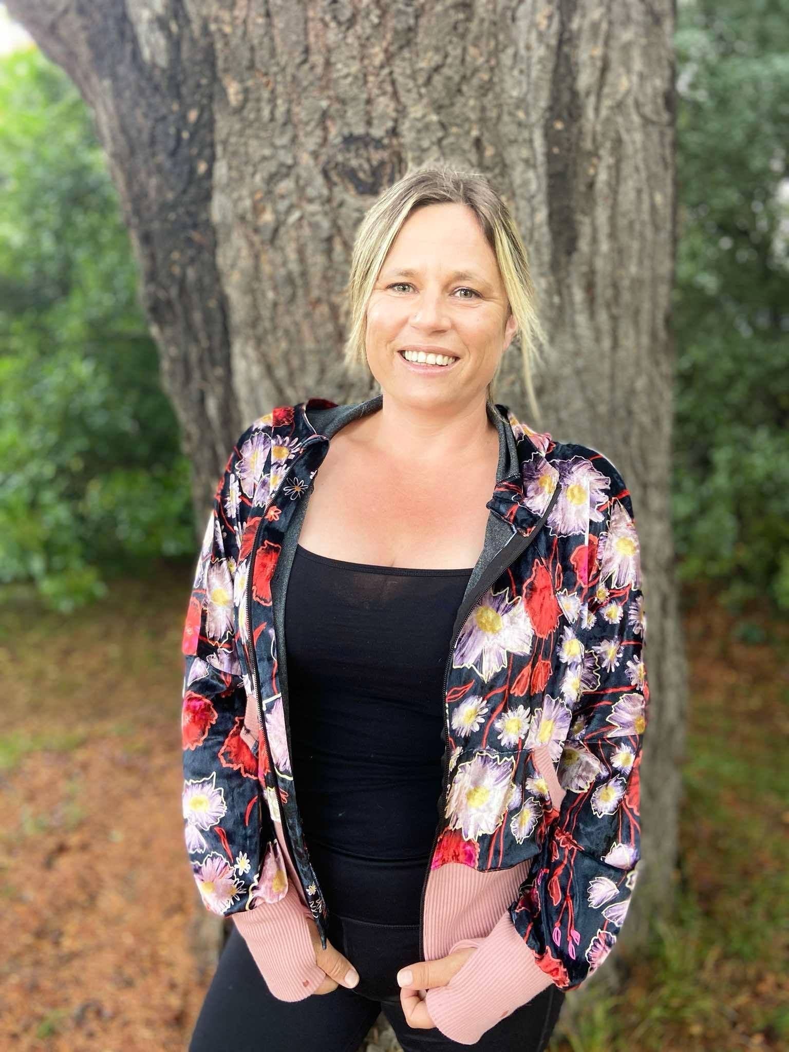 Woman outside modeling a bright floral athleisure hooded jacket with zip closure, kangaroo pocket detail, and thumbhole cuffs. Easy pdf sewing pattern.