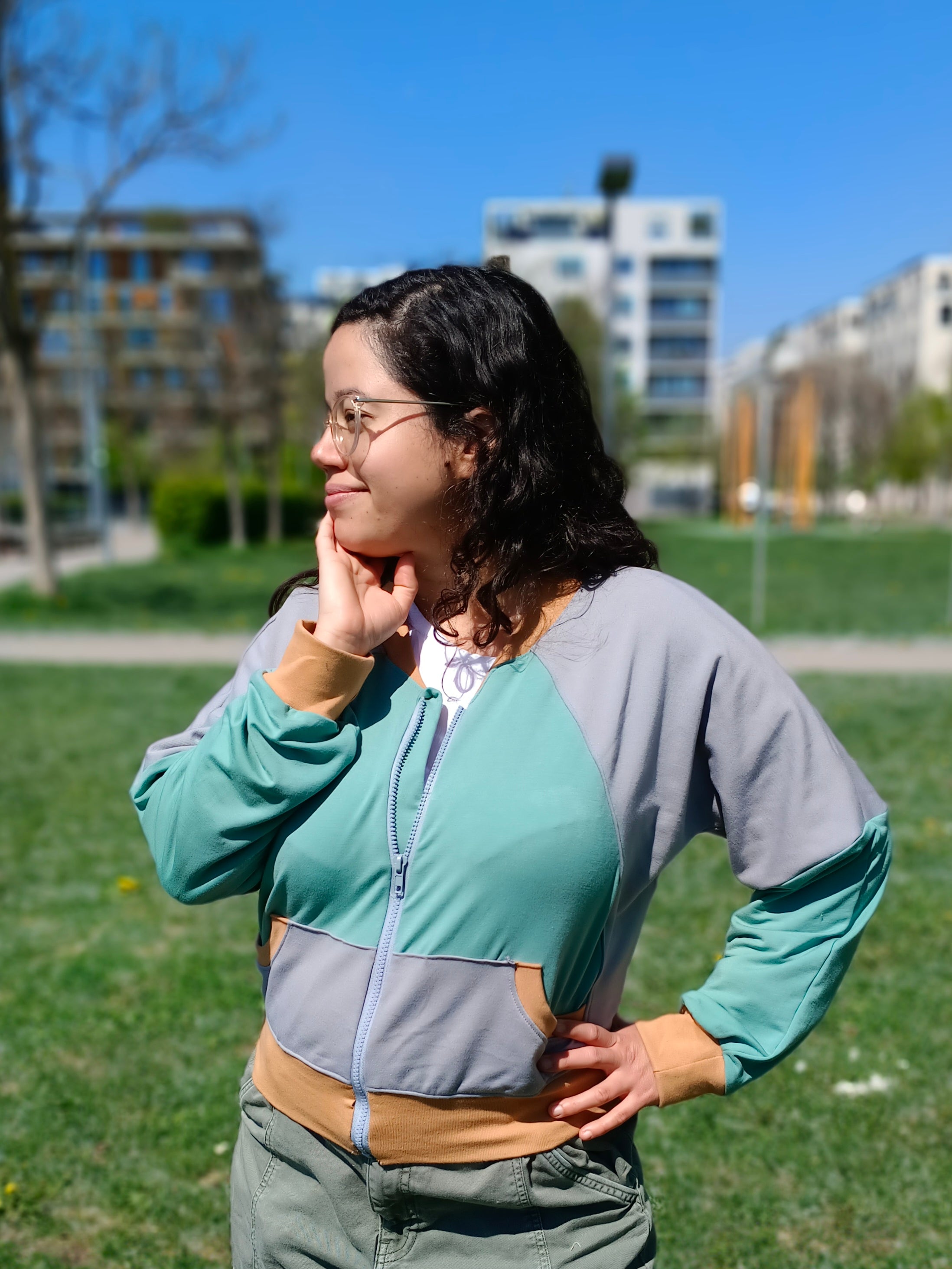 Woman outside modeling a color-blocked raglan bomber jacket with zip closure, kangaroo pocket detail, and cuffs. Easy pdf sewing pattern.