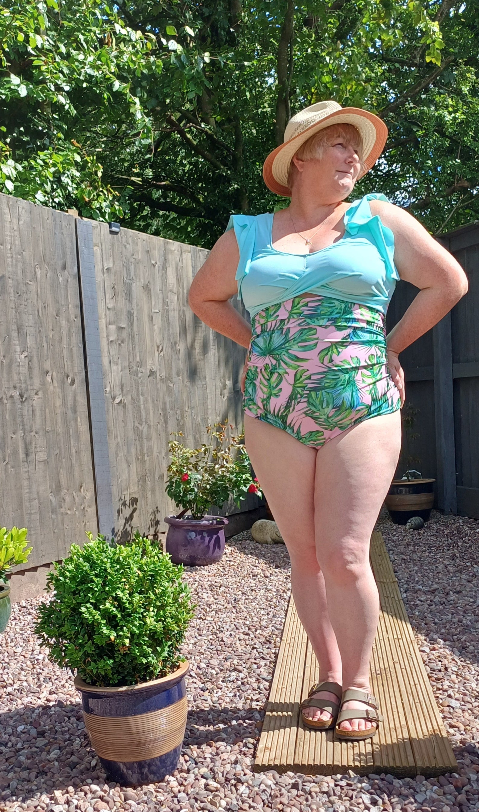 Person in a garden setting with plants and a hat modeling the tropical twist swimsuit pattern.