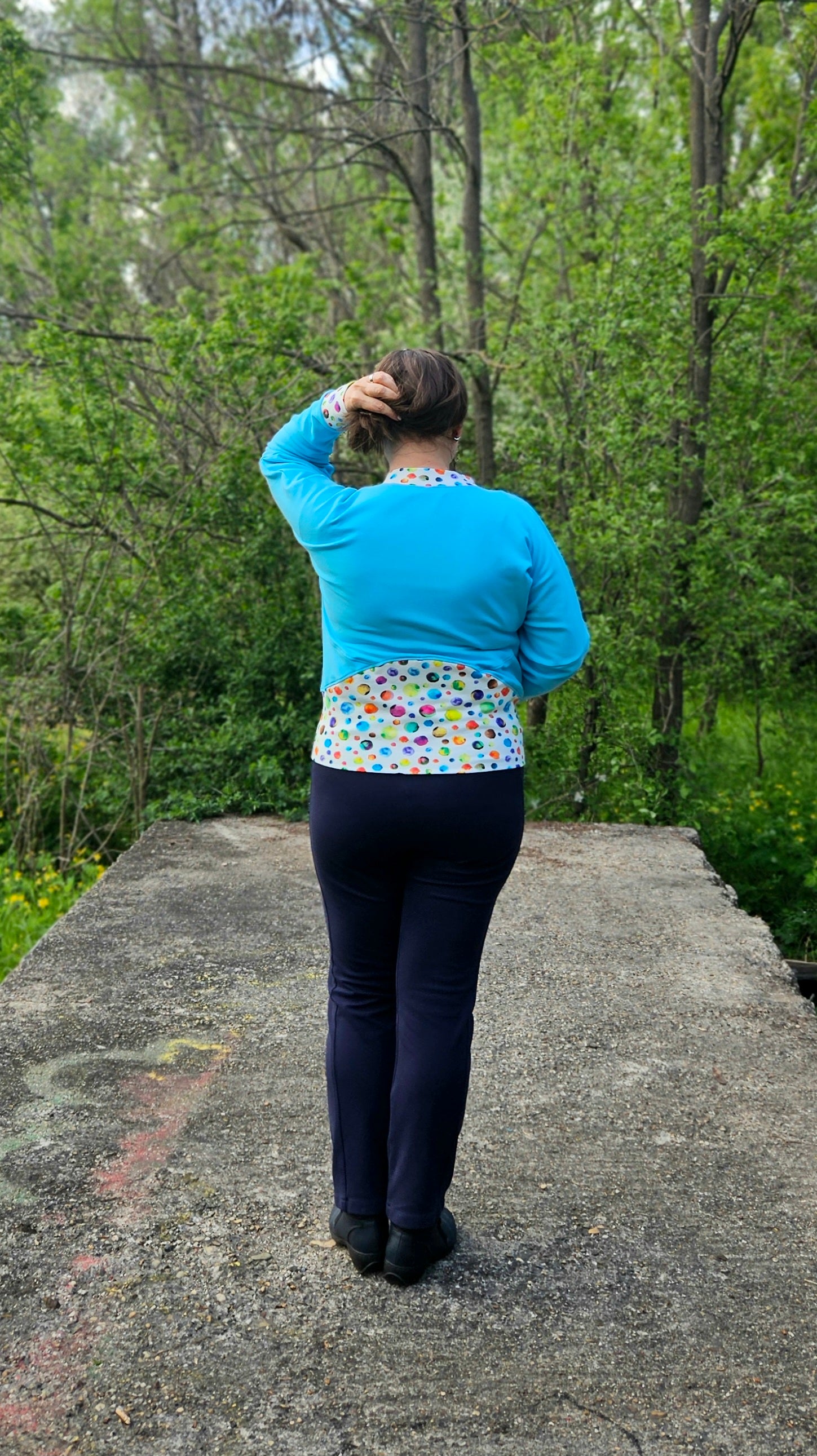 Woman on a path modeling a aqua and blue athletic bomber jacket with zip closure, kangaroo pocket detail, and cuffs. Easy pdf sewing pattern.