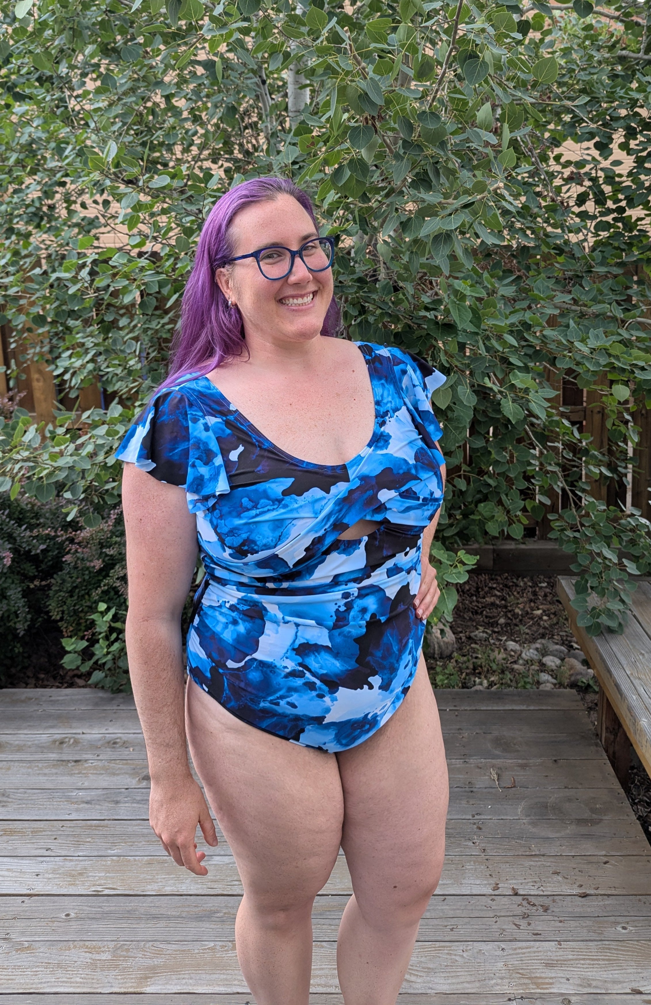 Woman in a swimsuit standing by a pool with trees and a building in the background