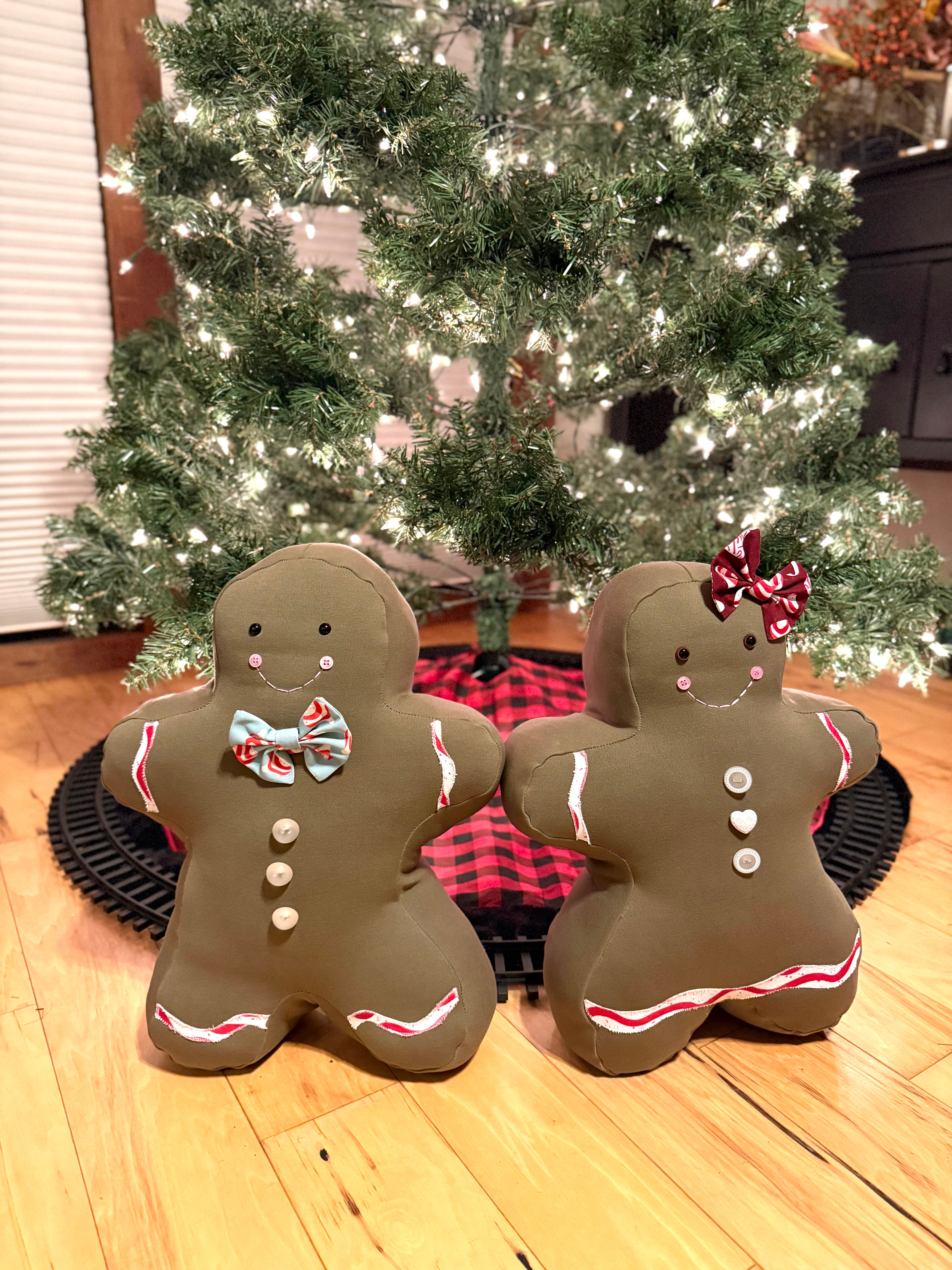 Two handmade gingerbread-themed decorative pillows in front of a Christmas tree.