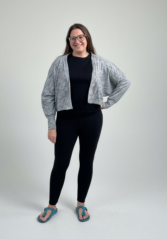 Person wearing a cropped gray sweater cardigan over a black top and leggings.