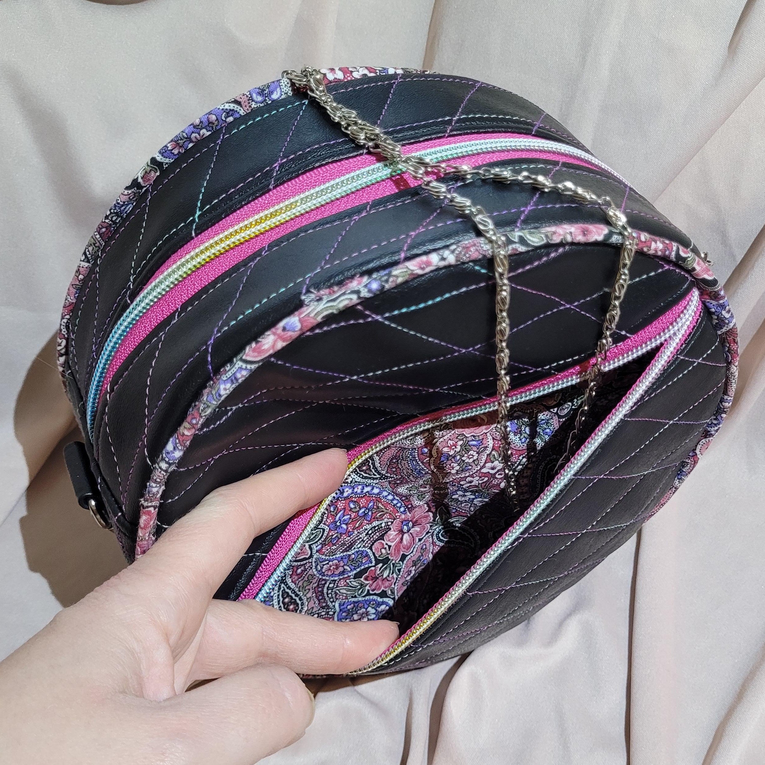 Hand holding a black quilted handbag with colorful accents on a beige fabric background