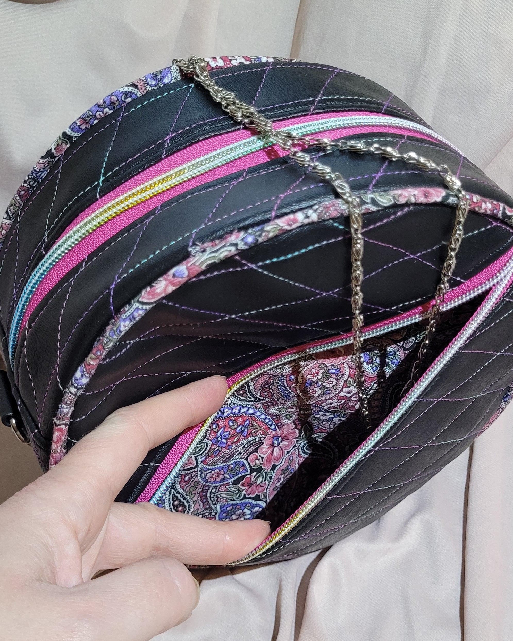 Hand holding a black quilted handbag with colorful accents on a beige fabric background